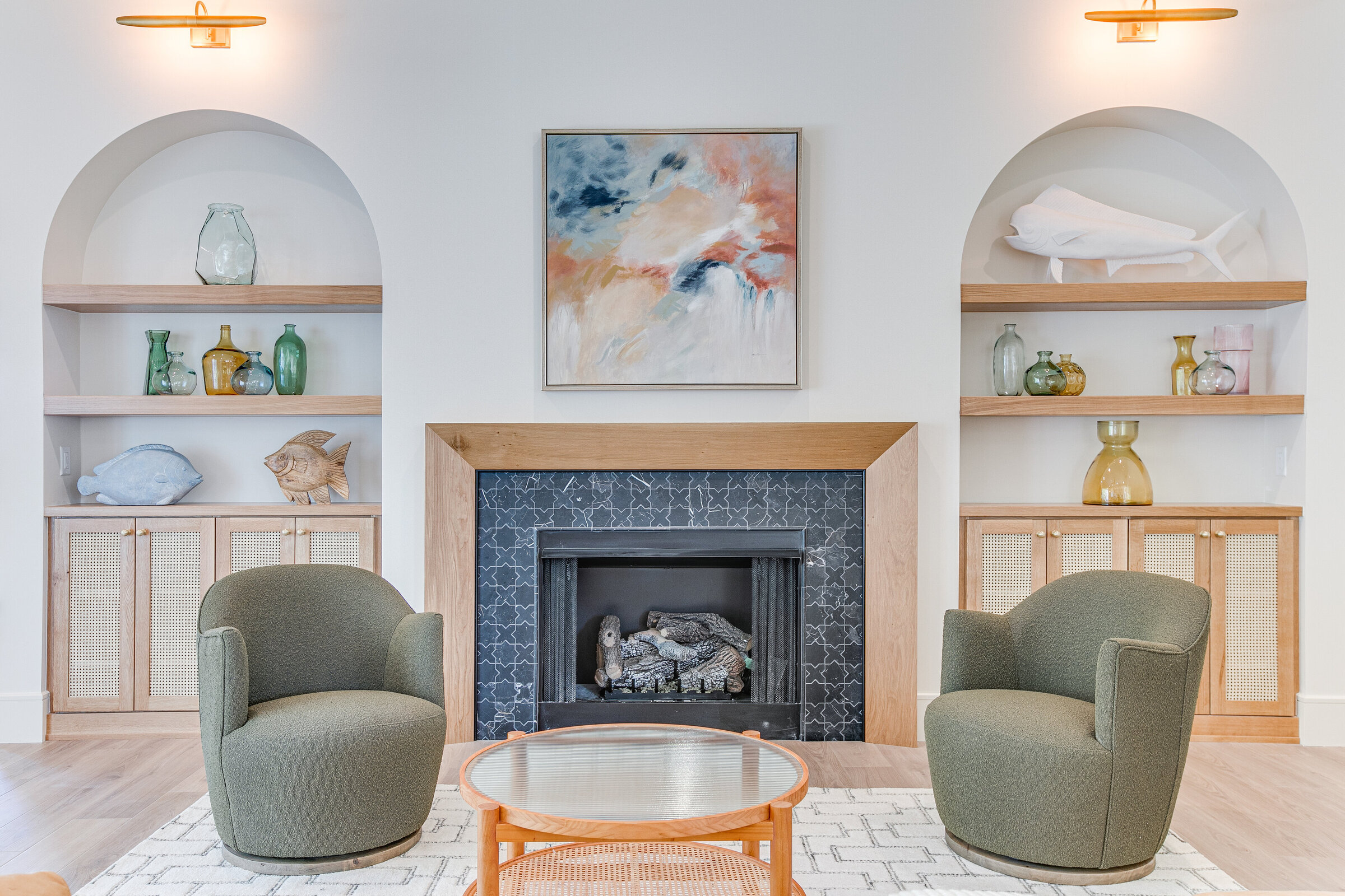 A beautifully designed sitting room featuring green swivel chairs, arched built-ins beside a custom-tiled fireplace, and high-end art hanging above. The space is well-lit, highlighting the luxurious and carefully curated details in this stunning long shore custom home.