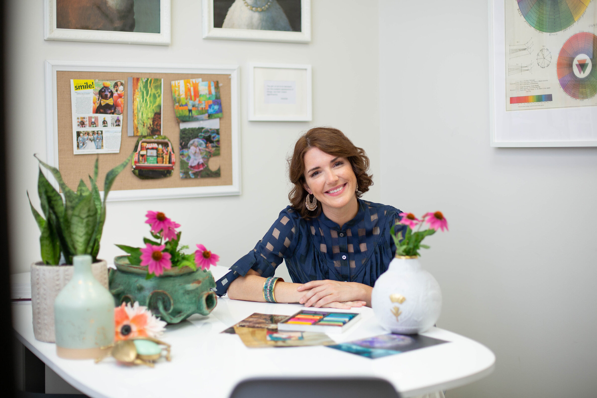 Woman smiling from behind a desk covered in flowers and art supplies