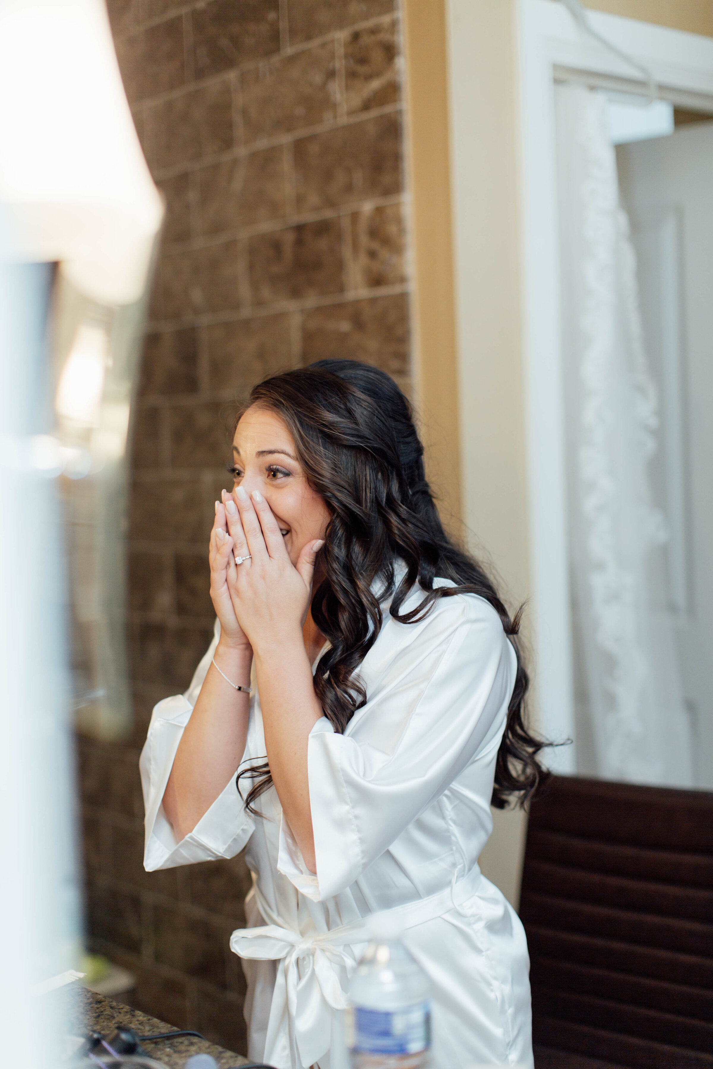 Bride looking surprised and delighted at her reflection after finishing her hairstyle.