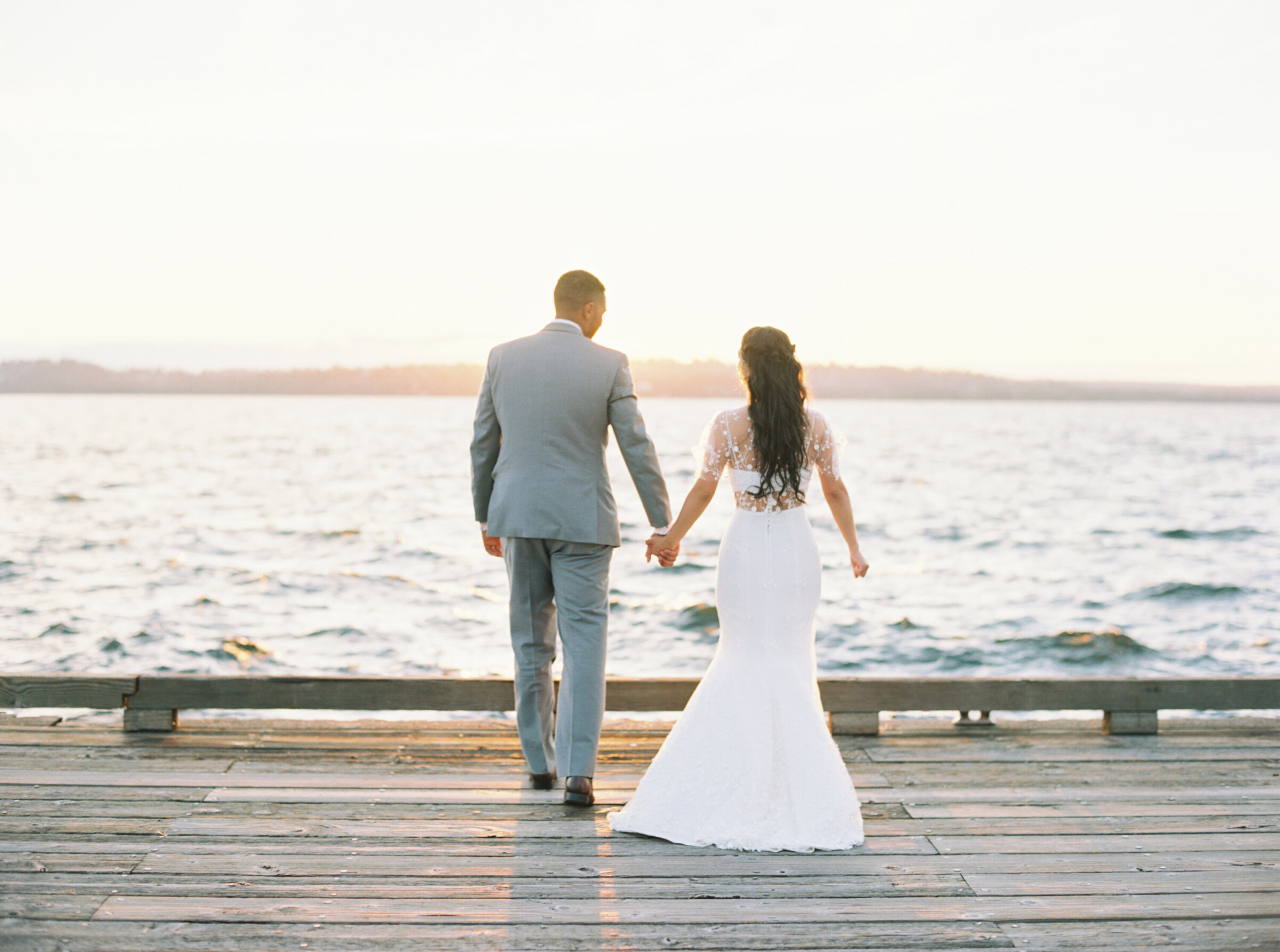 bride and groom walking away holding hands on dock at sunset