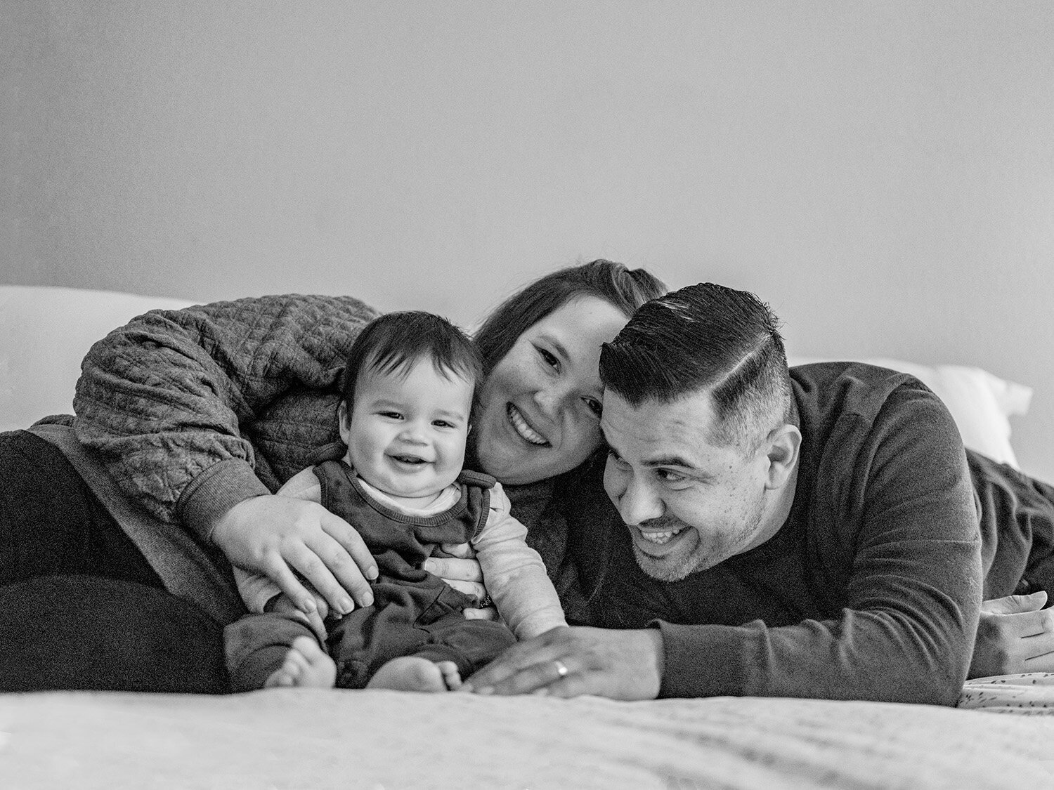 Natural in-home family photo of two parents holding their baby, taken in soft natural light in the San Francisco Bay Area