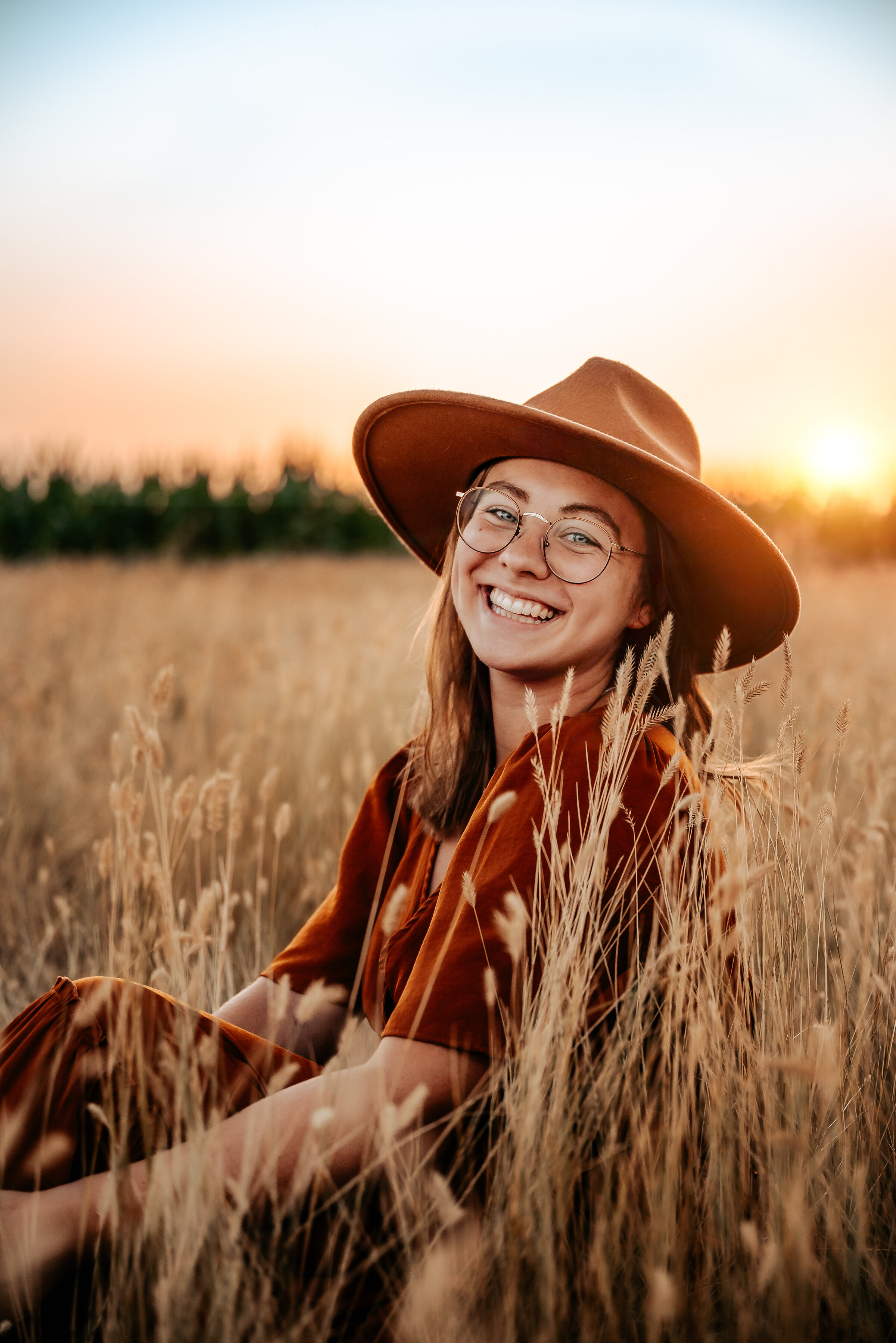 Woman smiles in field of tall grass while wearing a wide brim felt hat