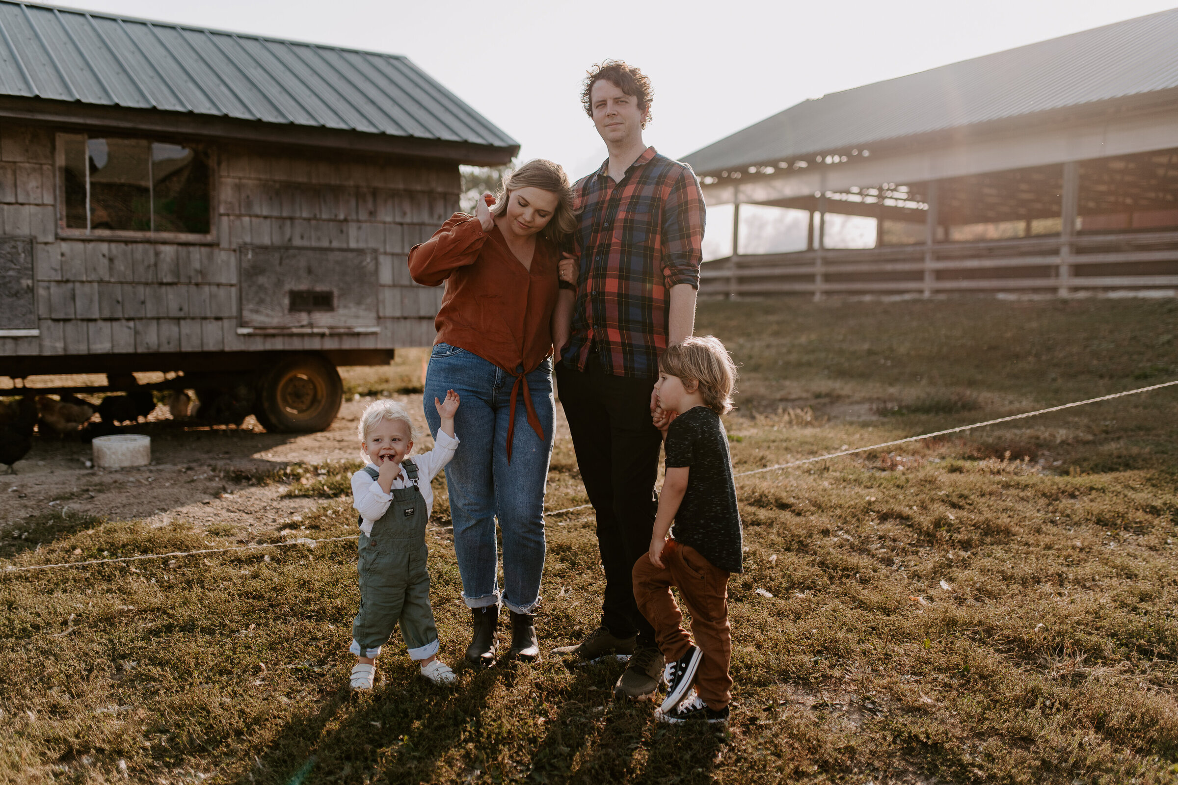 A mom, dad, and two children pose in front of a chicken coop.