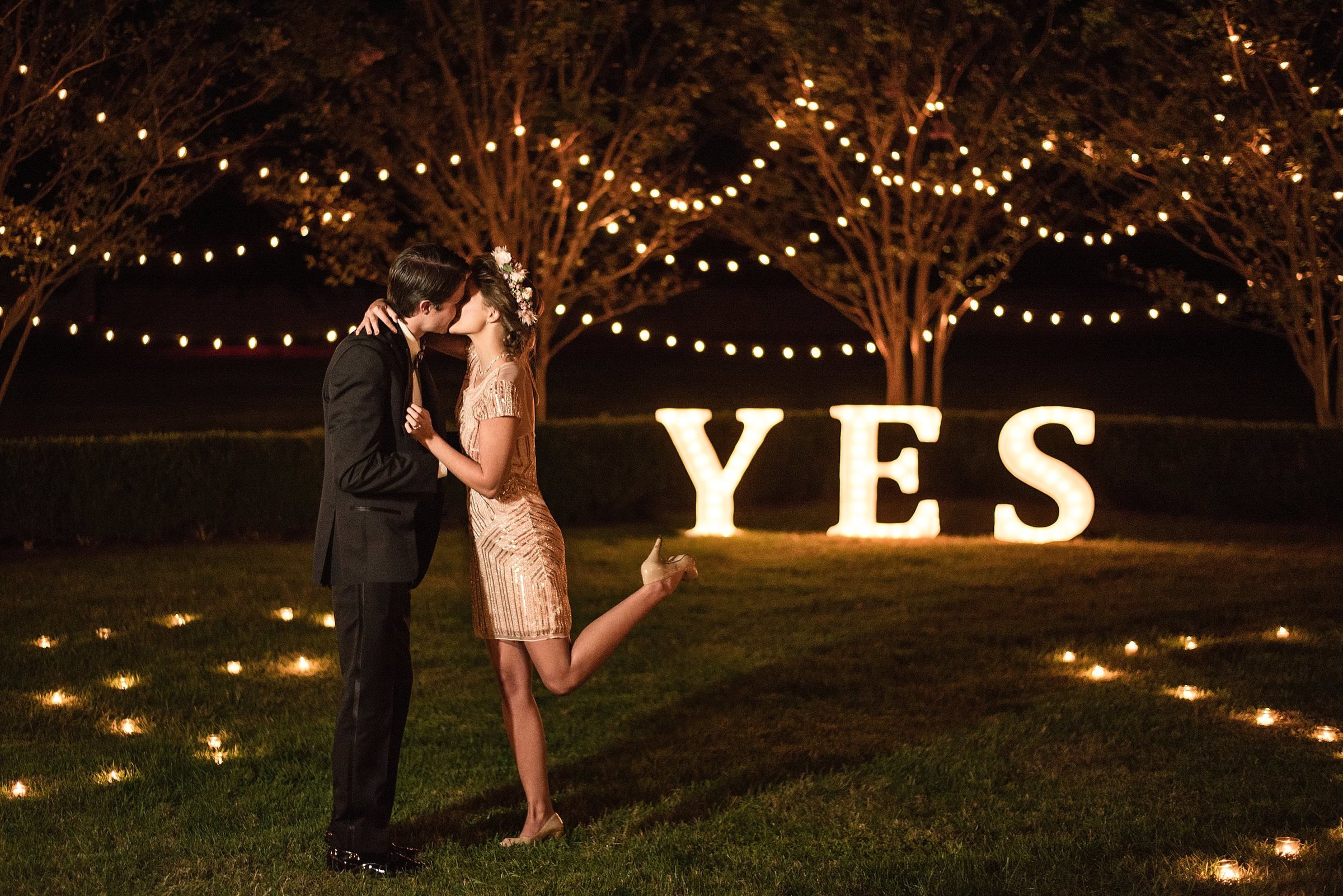 Proposal photo in the courtyard at Carnton with candlelit pathway and bistro light strung in the trees and oversized Yes letters lit in the background