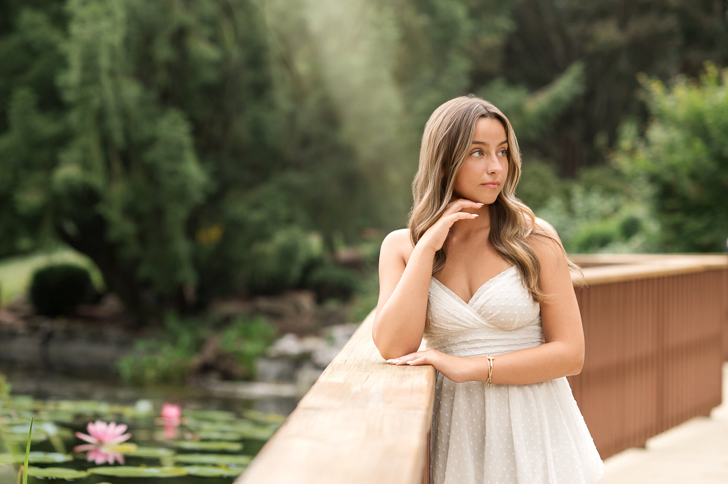Senior girl in white dress standing on a flower-lined path during a Hershey Gardens photo session near York, Harrisburg, and Lancaster PA.