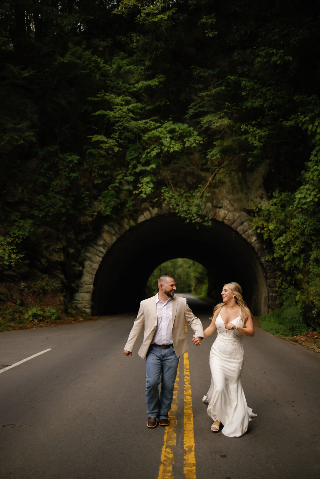 elope to Gatlinburg planner has bride and groom holding hands and runs down a road together under a tunnel