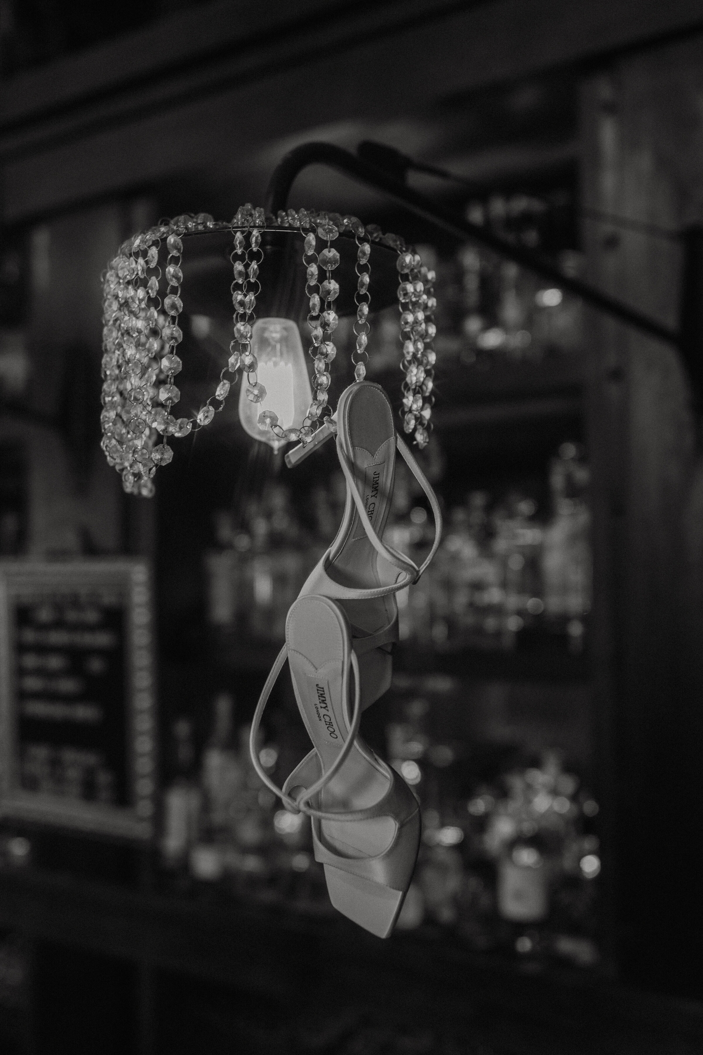 black and white photo of a pair of jimmy choo white heels hanging from a  chandelier