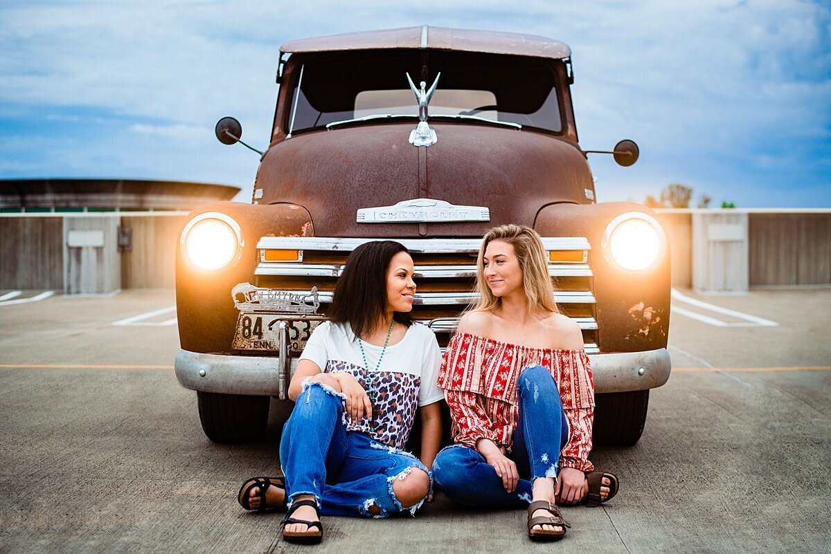 Two best friends sitting in front of a vintage truck at sunset for their senior photos