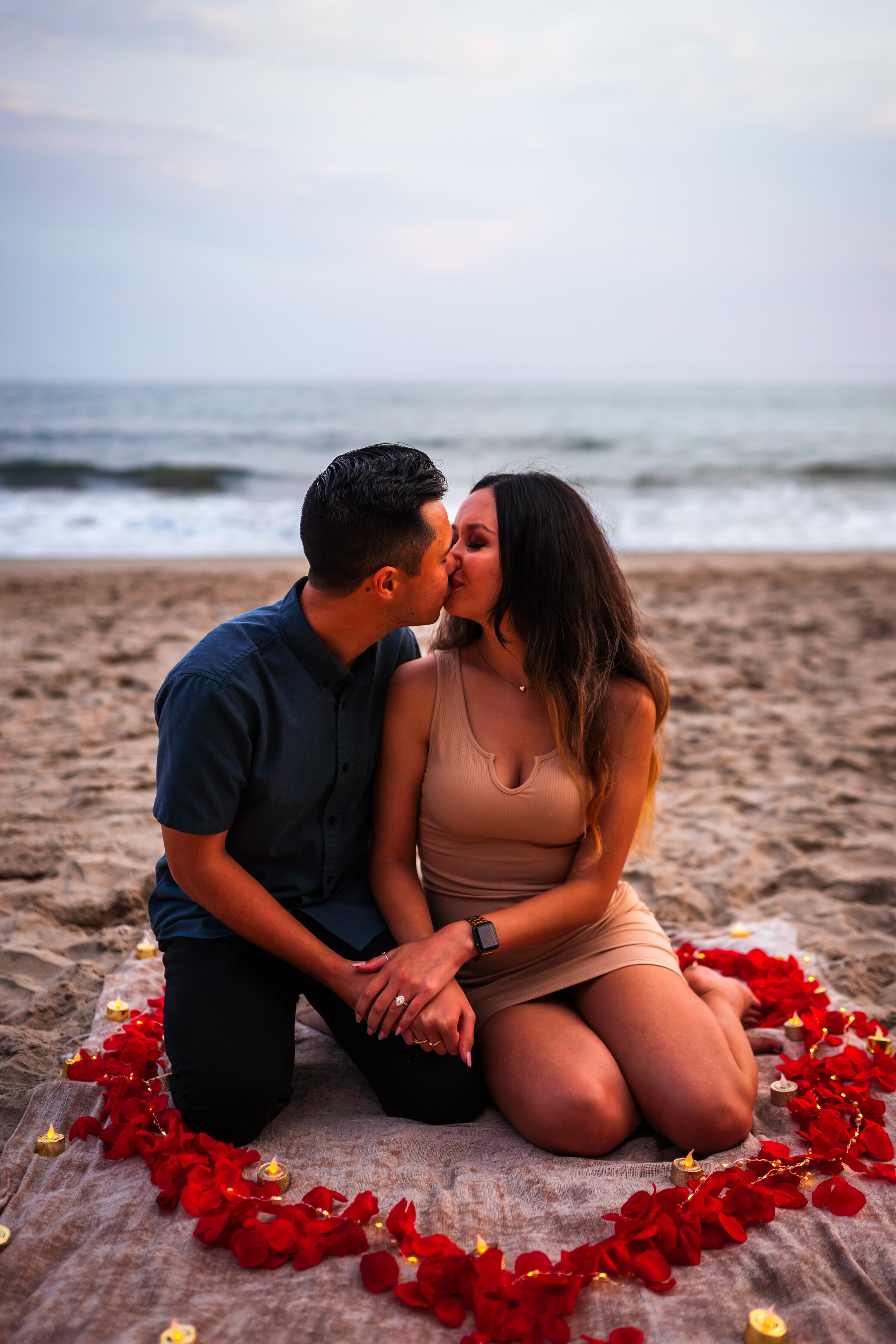 A couple sitting on the beach inside a heart made of rose petals