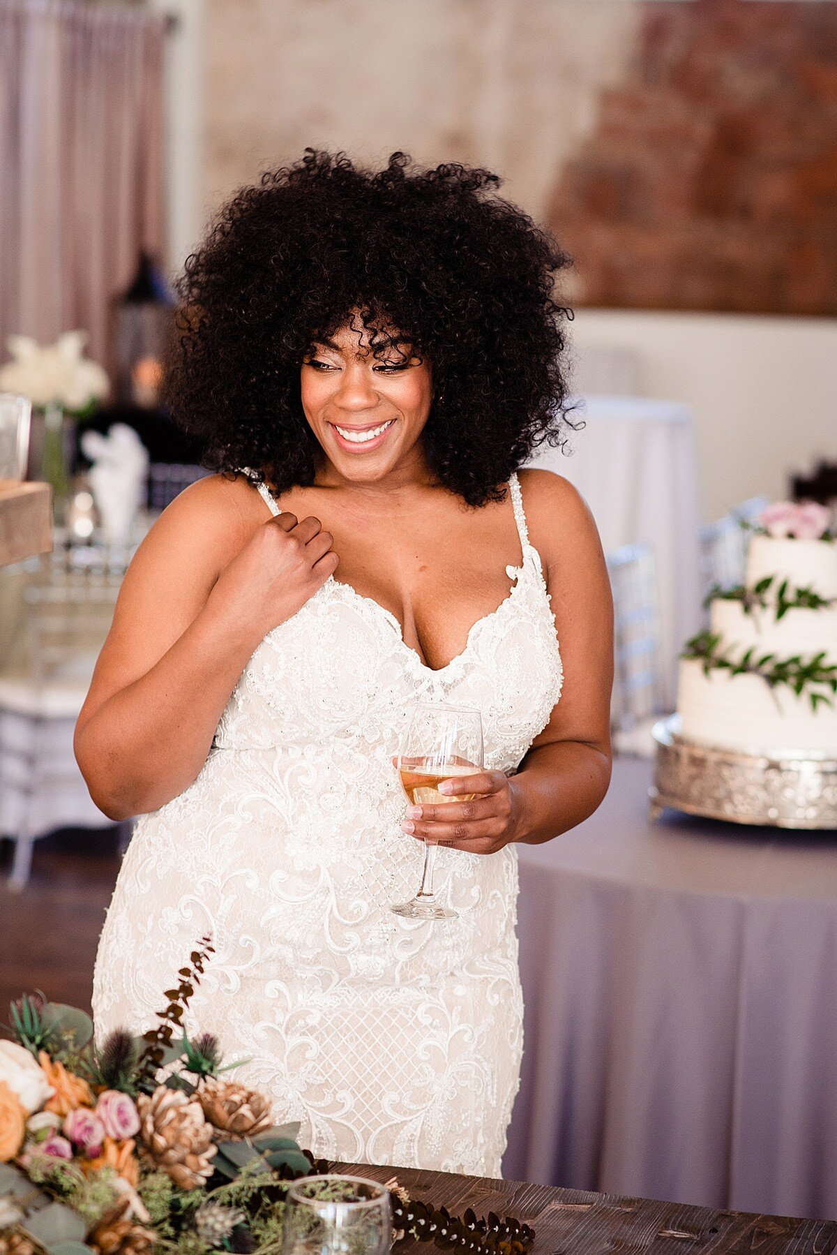 Bride holding a glass of wine wearing a lace wedding dress with thin straps at reception