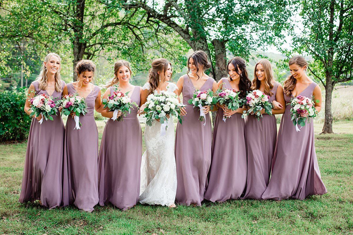 Bridesmaids wearing lilac wedding dresses carrying their bouquets and walking with bride outside