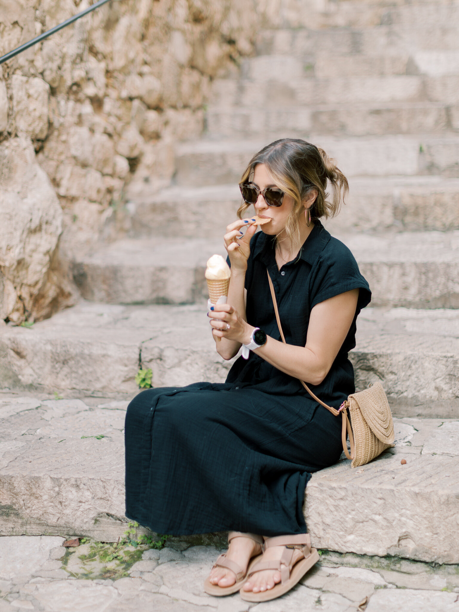 Little Rock photographer Bailey Feeler in black dress and sunglasses sits on step eating gelato