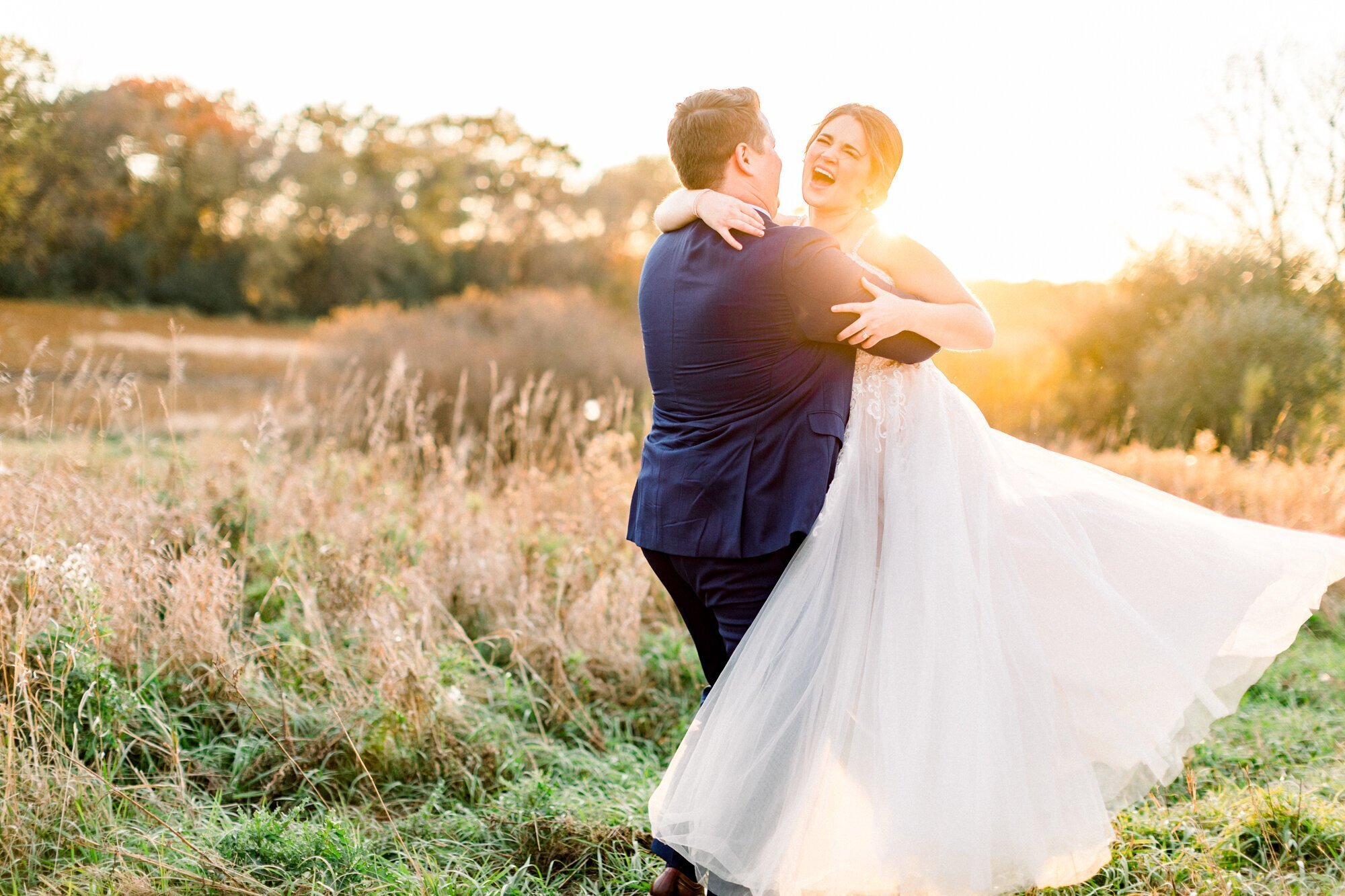 Groom lifting and spinning bride in a field, taken by wedding photographers minneapolis