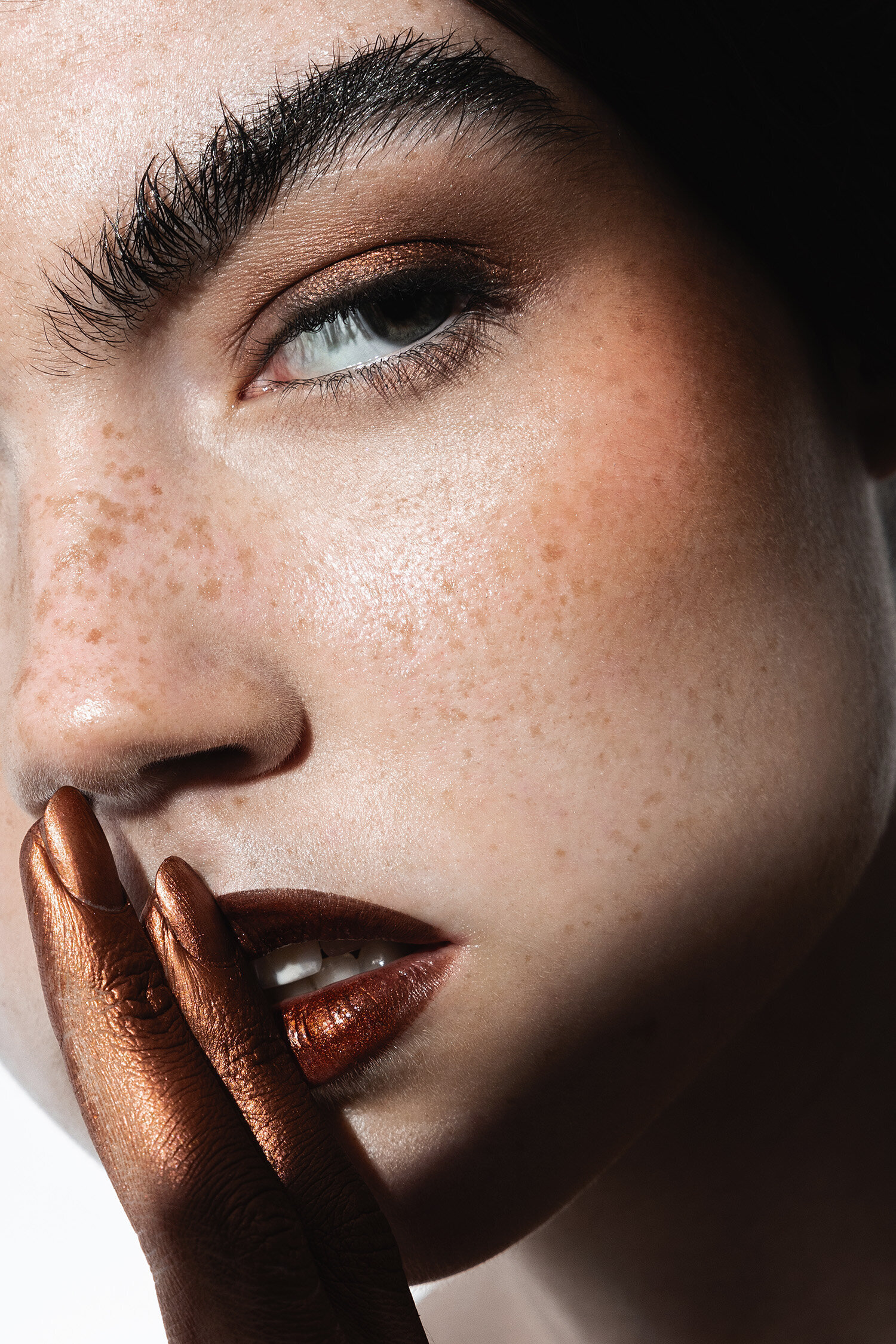 Beauty photography portrait with freckles, metallic rust lips and eyeshadow in shhh gesture