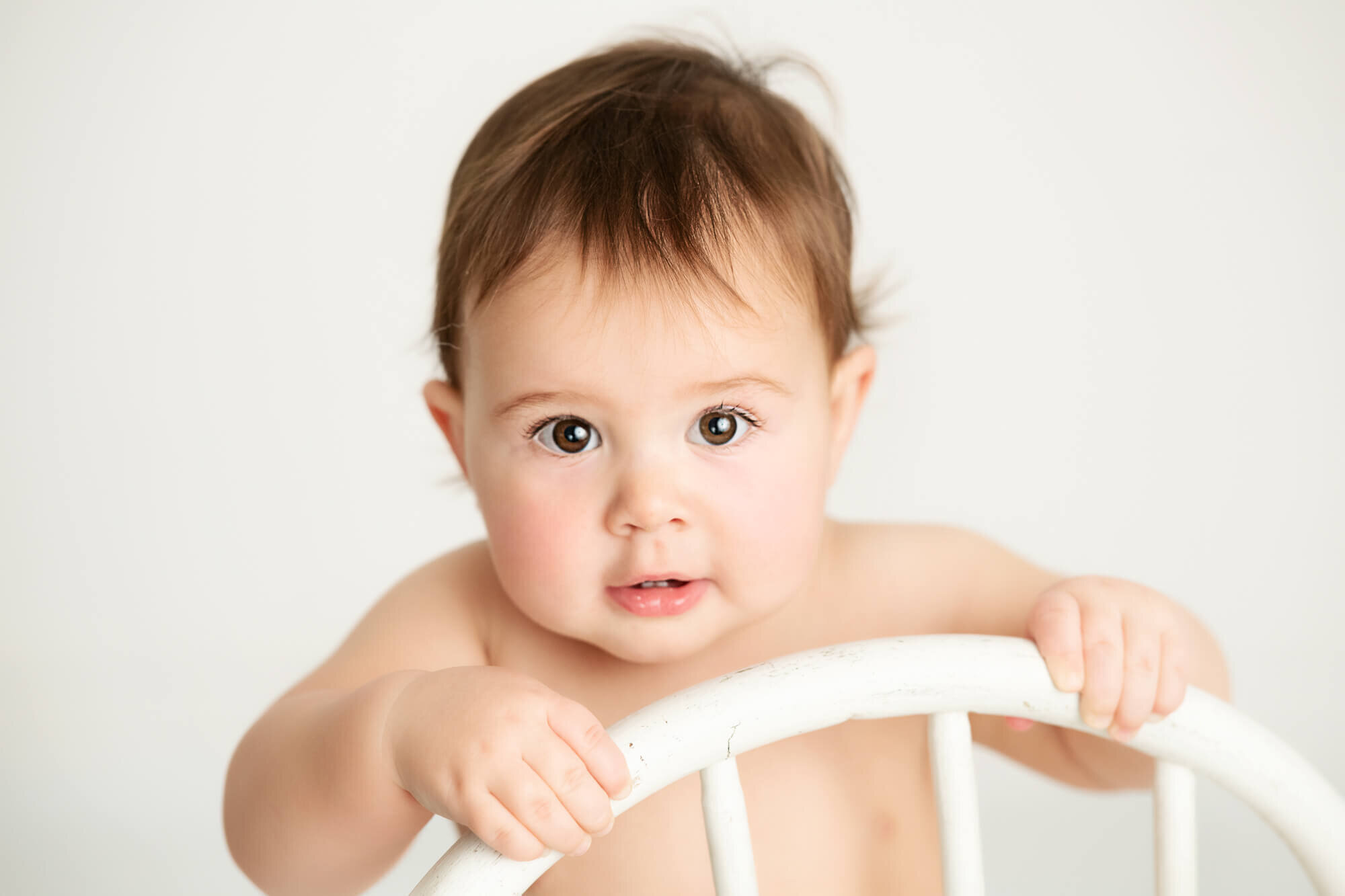 Chubby baby boy standing holding chair