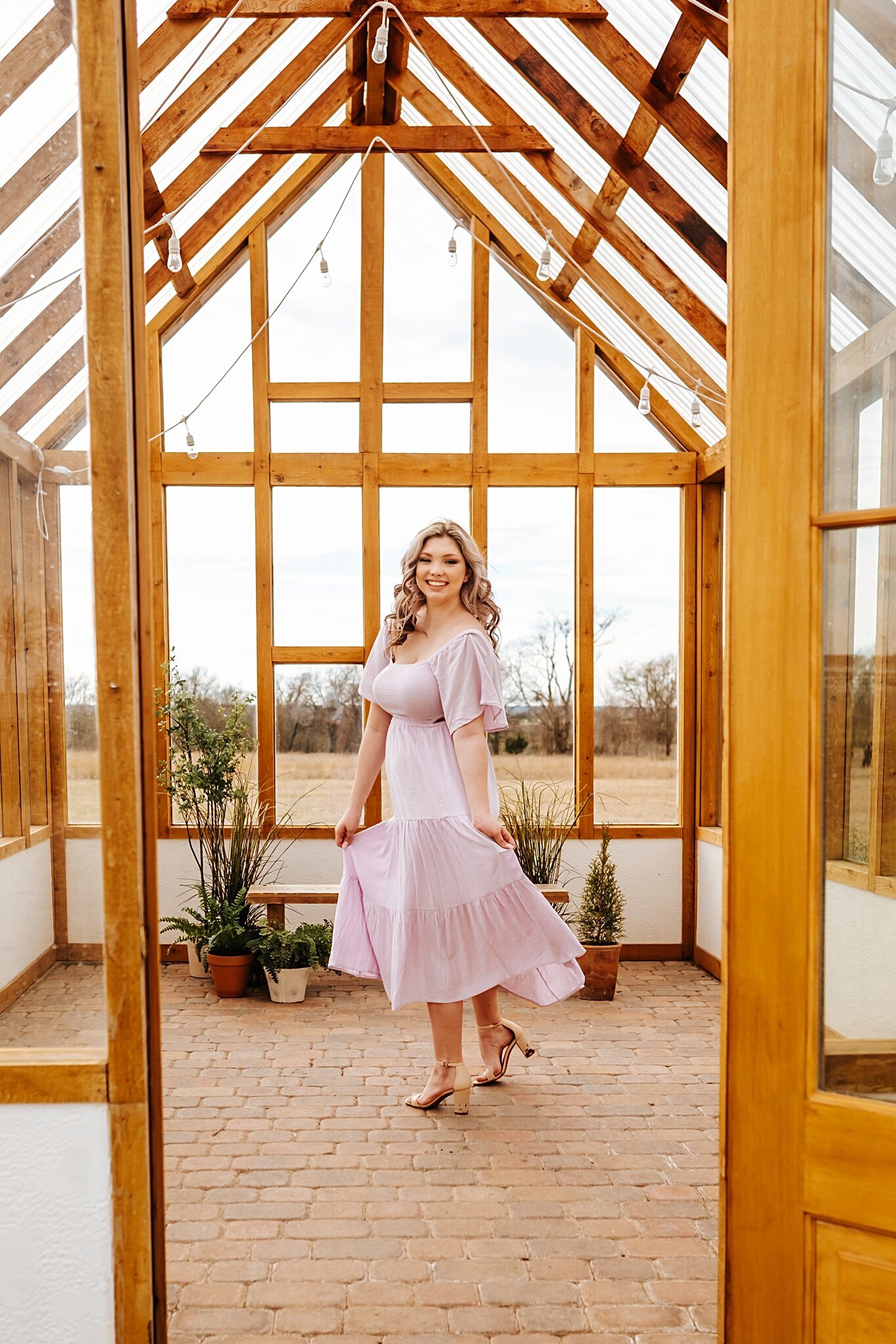 Seattle senior girl spinning in a greenhouse at Stem and Light studio, she is wearing a dress from Shop Morning Lavender
