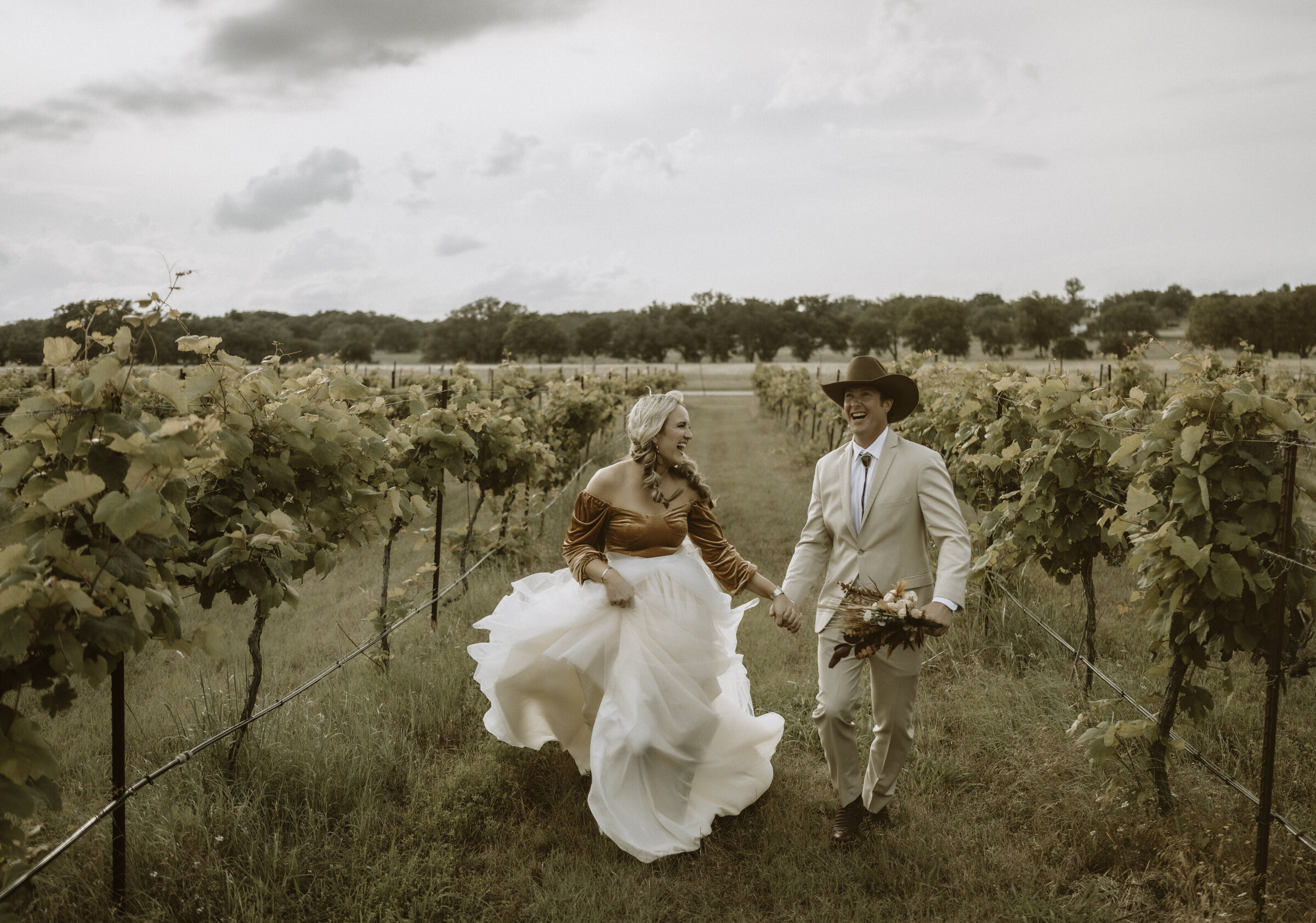 couple running through grape vine field on their wedding day in florence