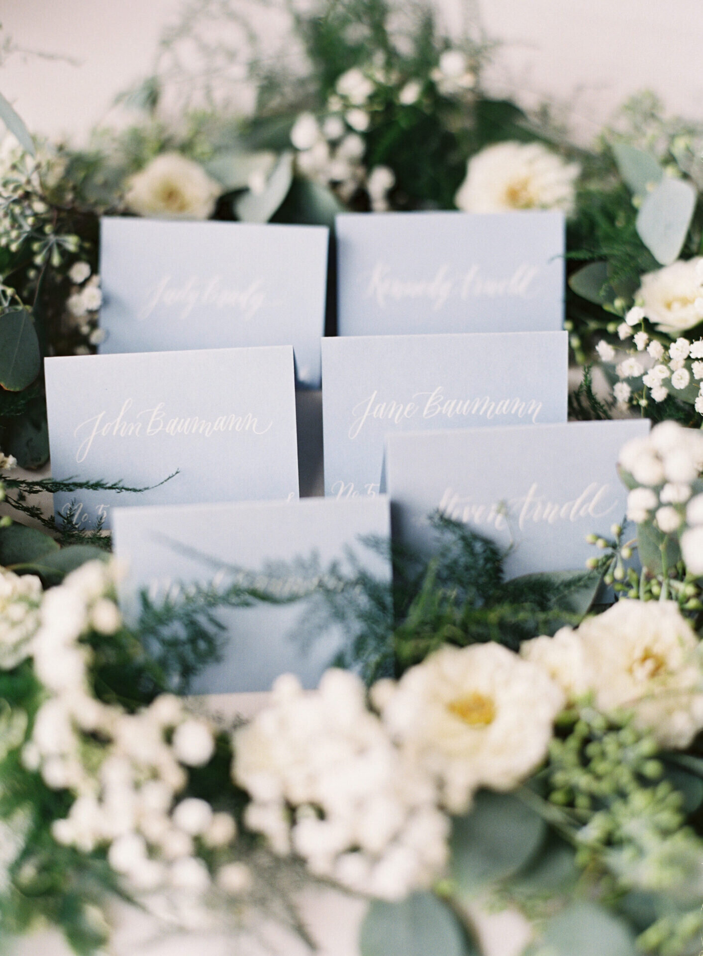blue placecards at wedding table with white and green florals surrounding them