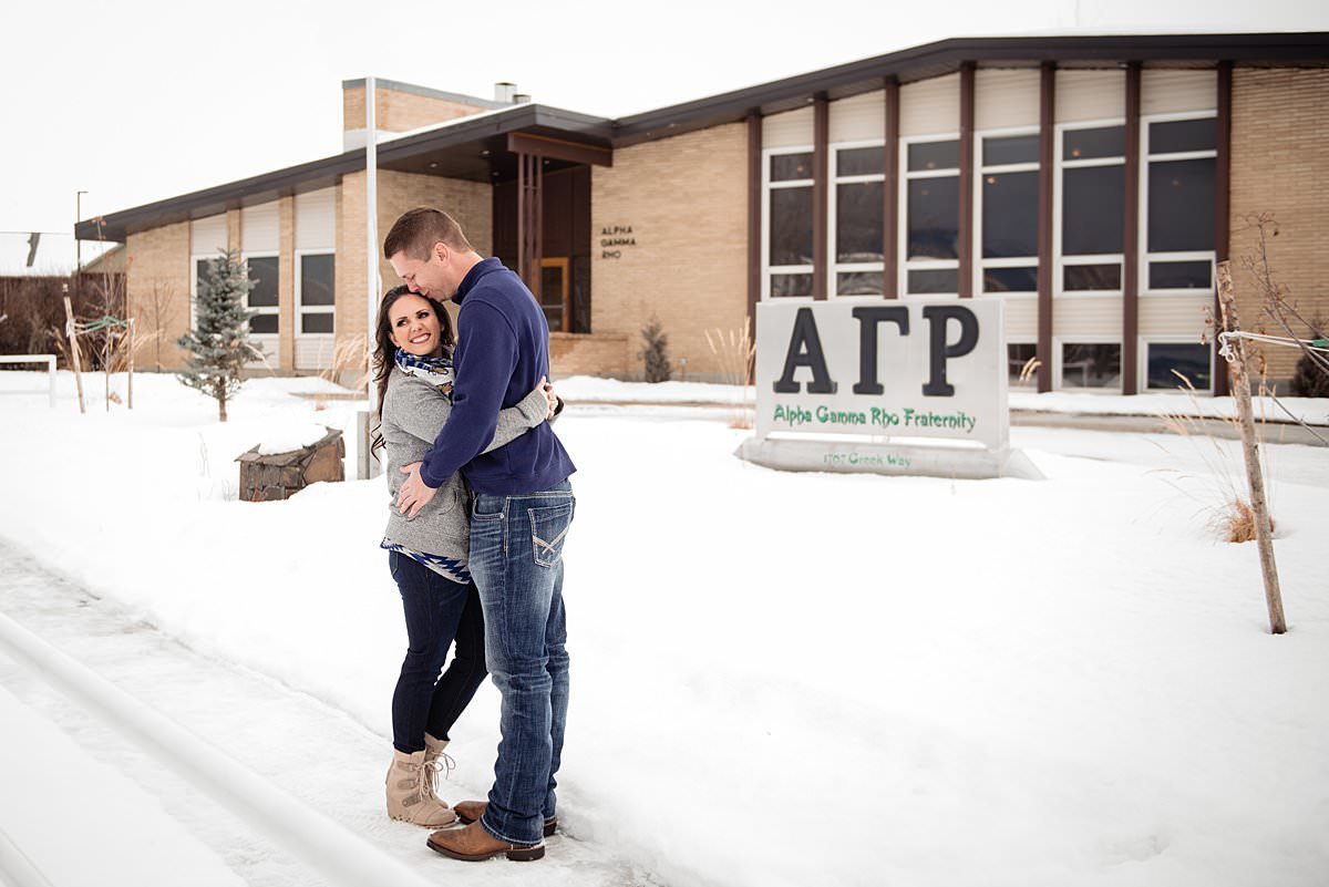 Engaged couple standing outside of the Alpha Gamma Rho chapter house at Montana State University with snow covered grounds