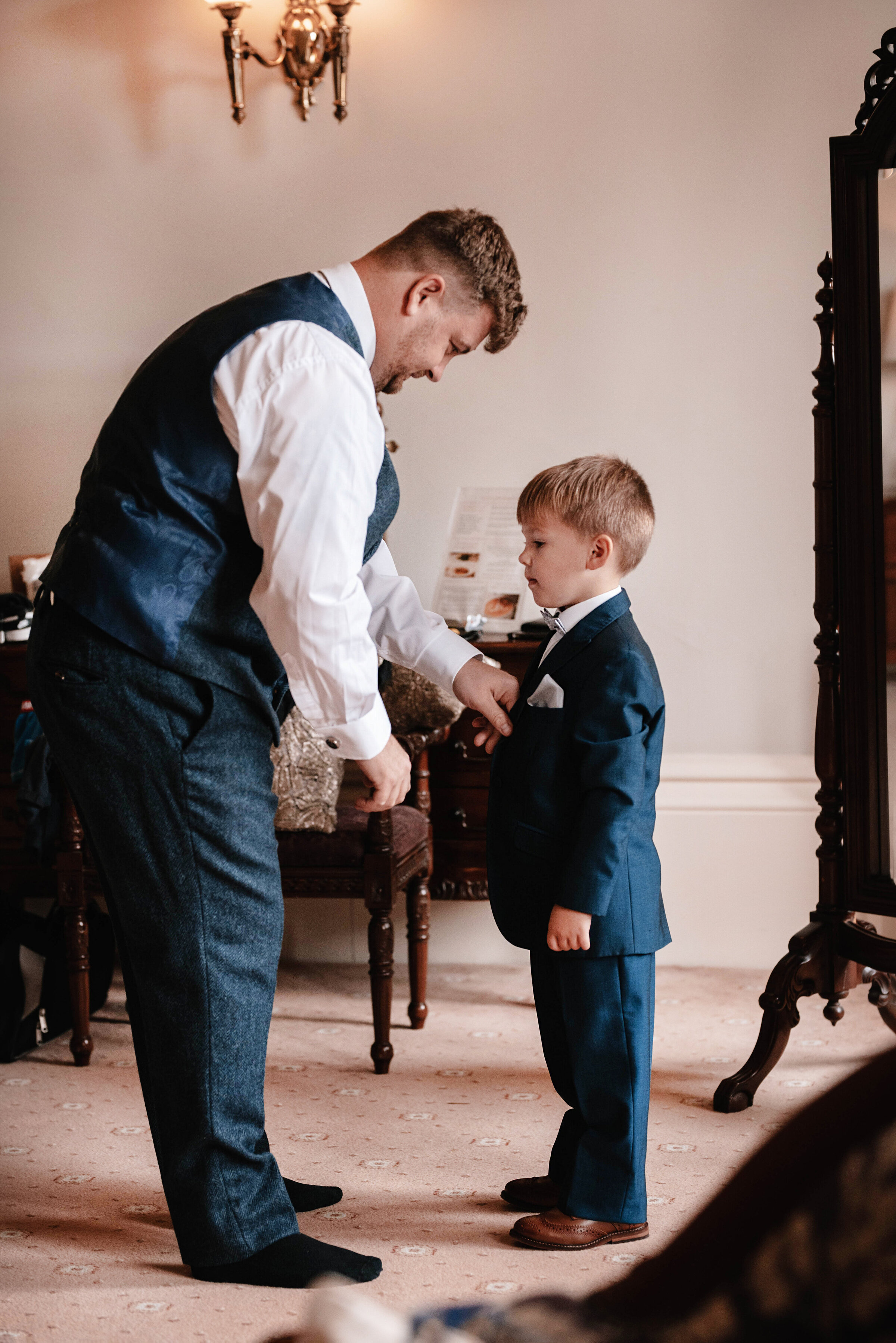 Groom dressed in wedding suit helping his son fasten his suit buttons