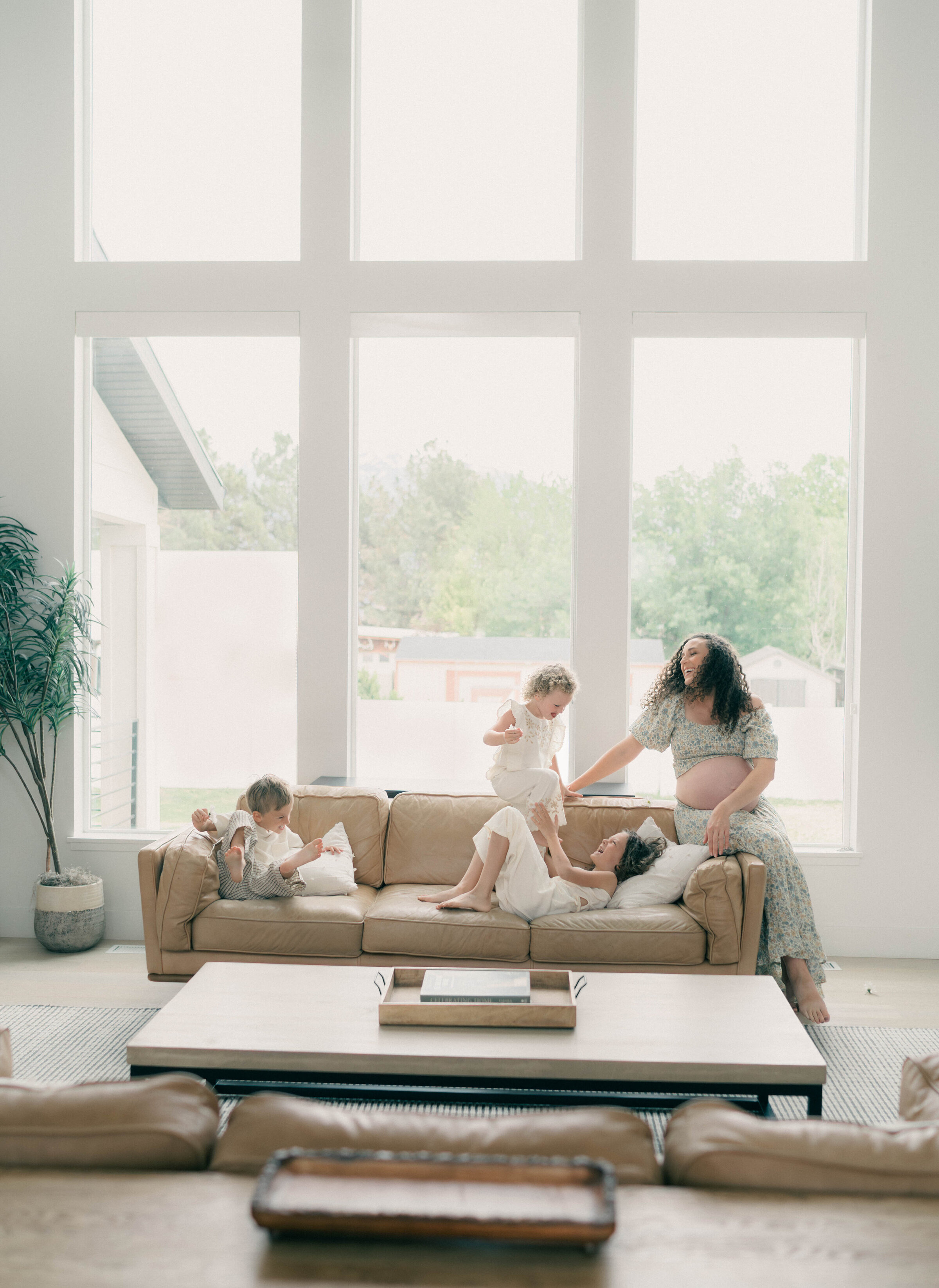 Playful at-home maternity session in bright living room with mom and toddlers, captured in soft natural light by newborn photographer in Utah