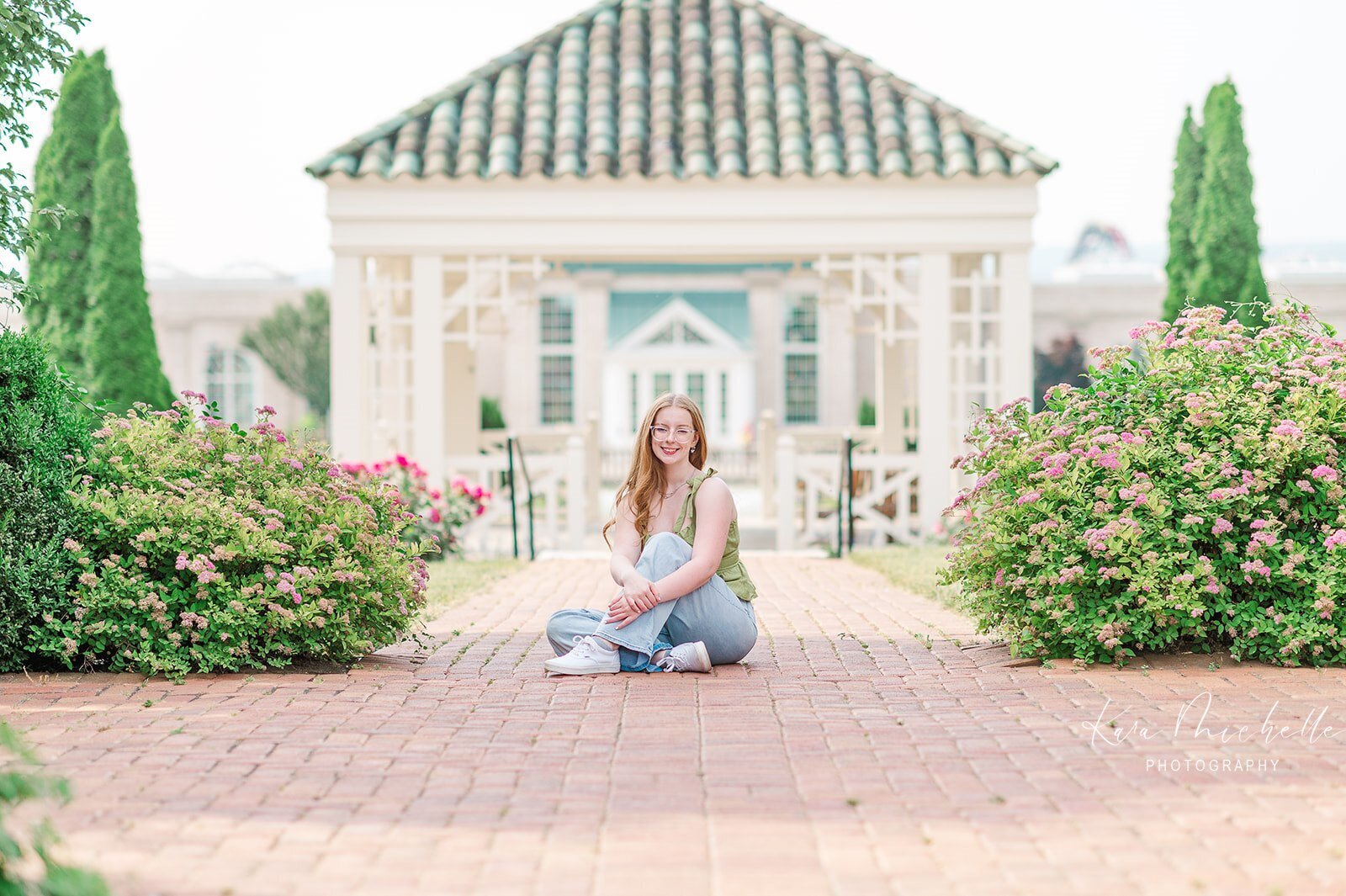 Senior girl sitting on brick path in front of the white pavilion at Hershey Gardens in Hershey, PA