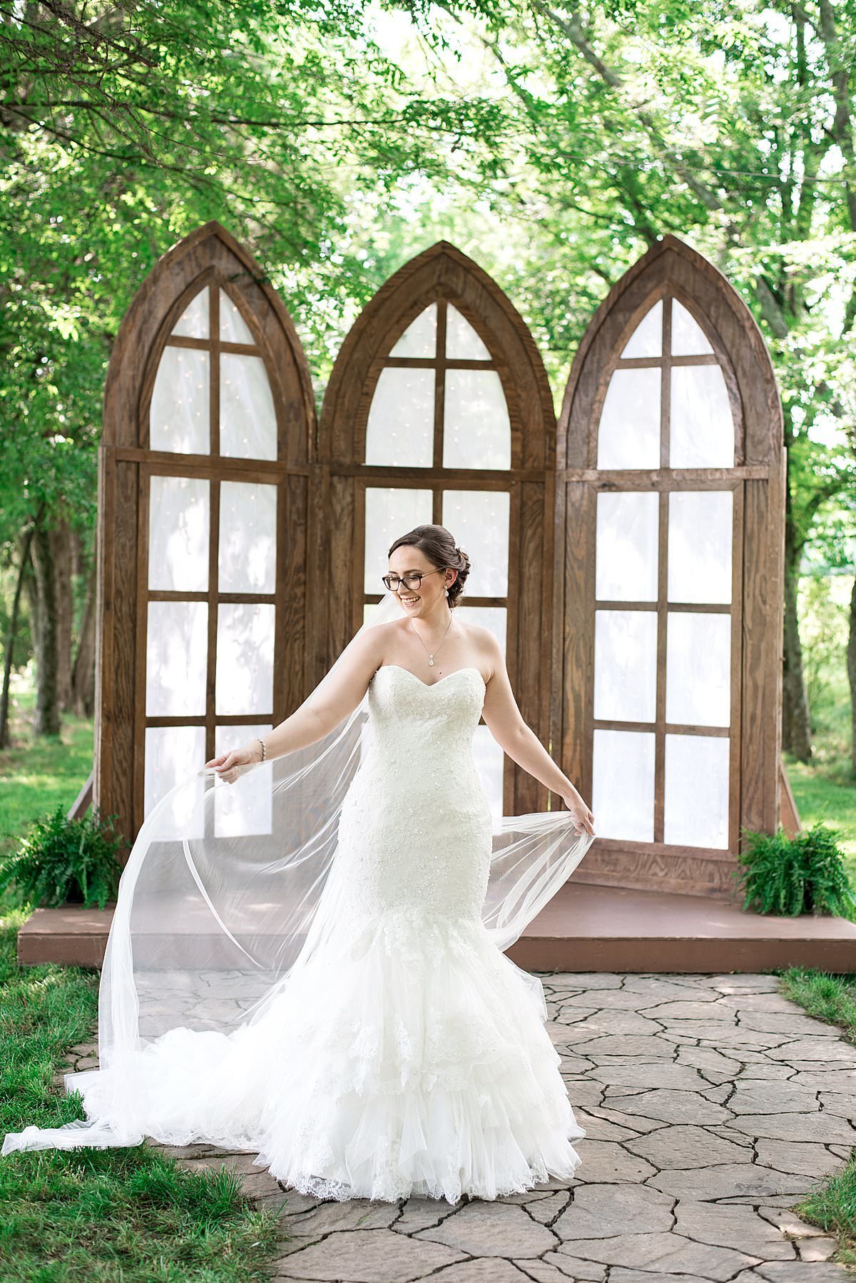 Bride wearing strapless sweetheart neckline dress with fit and flare frilly bottom and cathedral veil in front of large outdoor windows at Lovers Lane at Grace Valley Farm