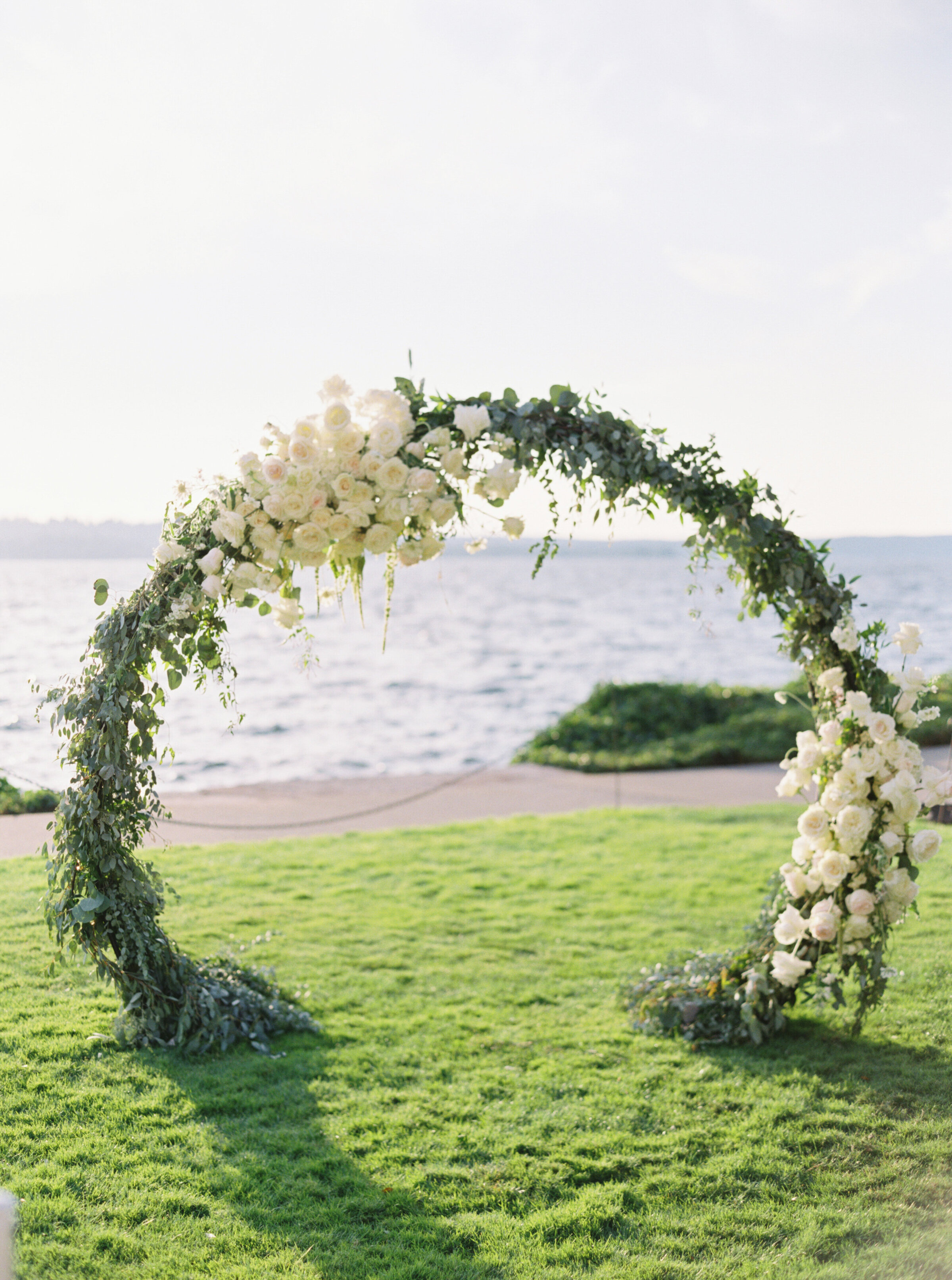 white rose and greenery rounded ceremony arch on the lake