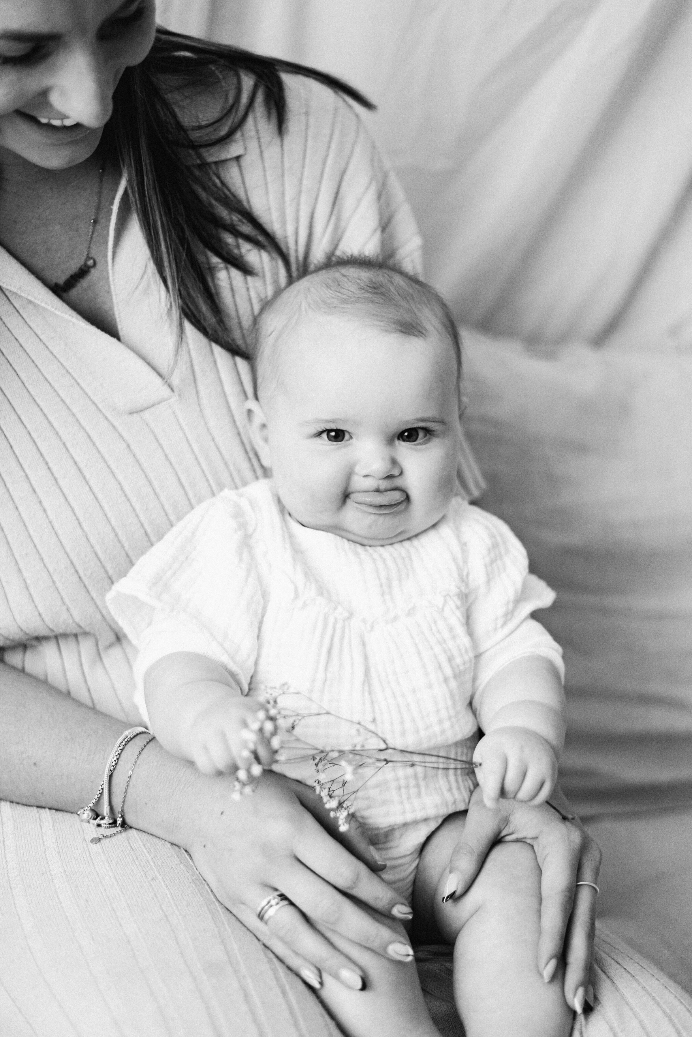 Little girl sitting on her mums lap sticking her tongue out at milestone photoshoot in Billingshurst