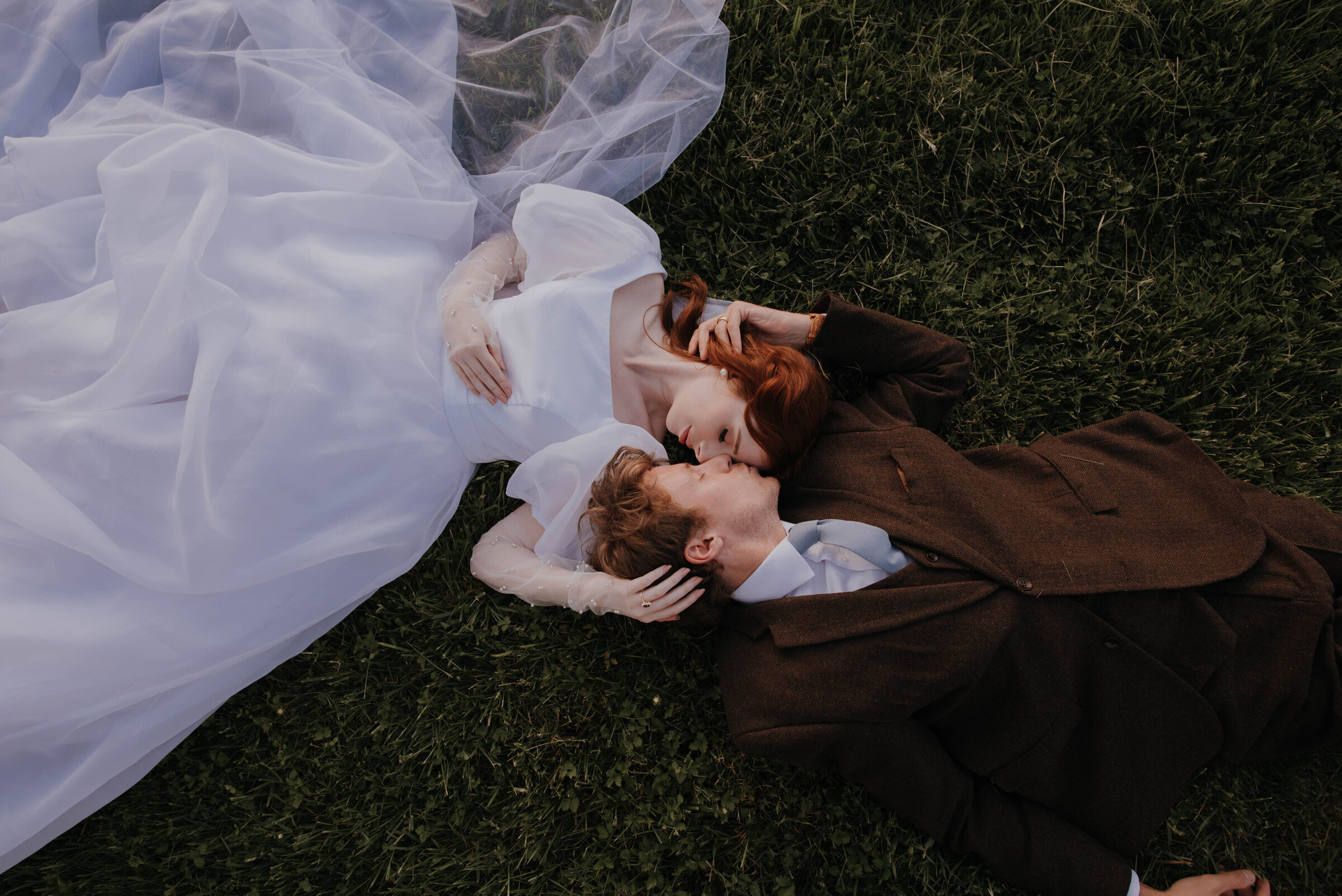 bride and groom laying on grass nose to nose