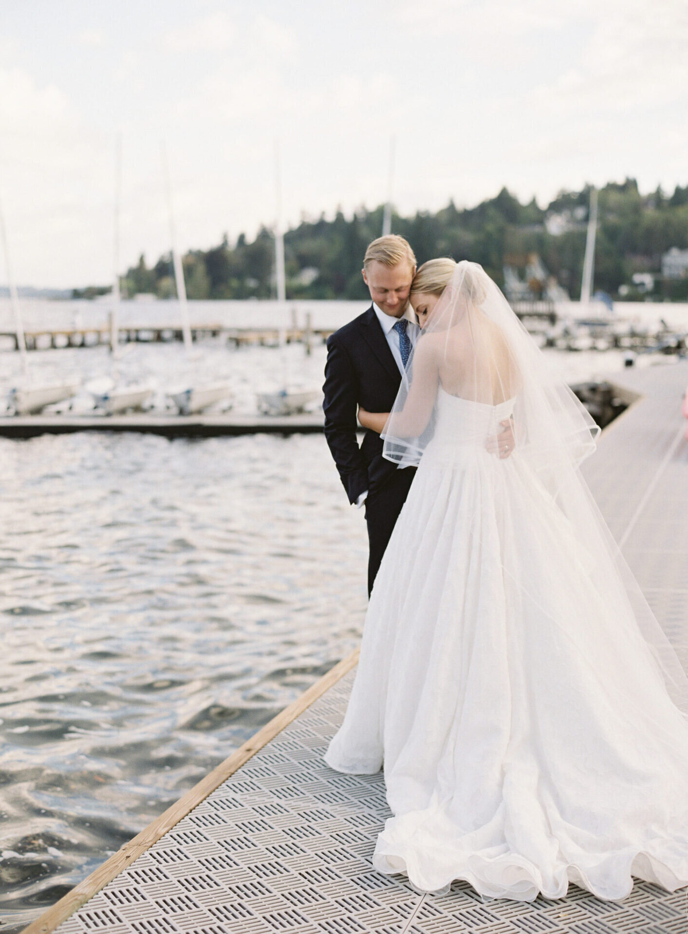 bride lays on her grooms shoulder cuddling on dock at dusk