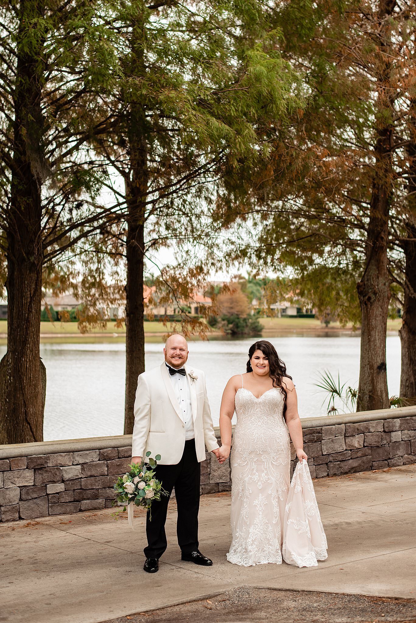 Groom wearing ivory jacket and black bow tie holding his wives hand in front of a pond at an Orlando country club