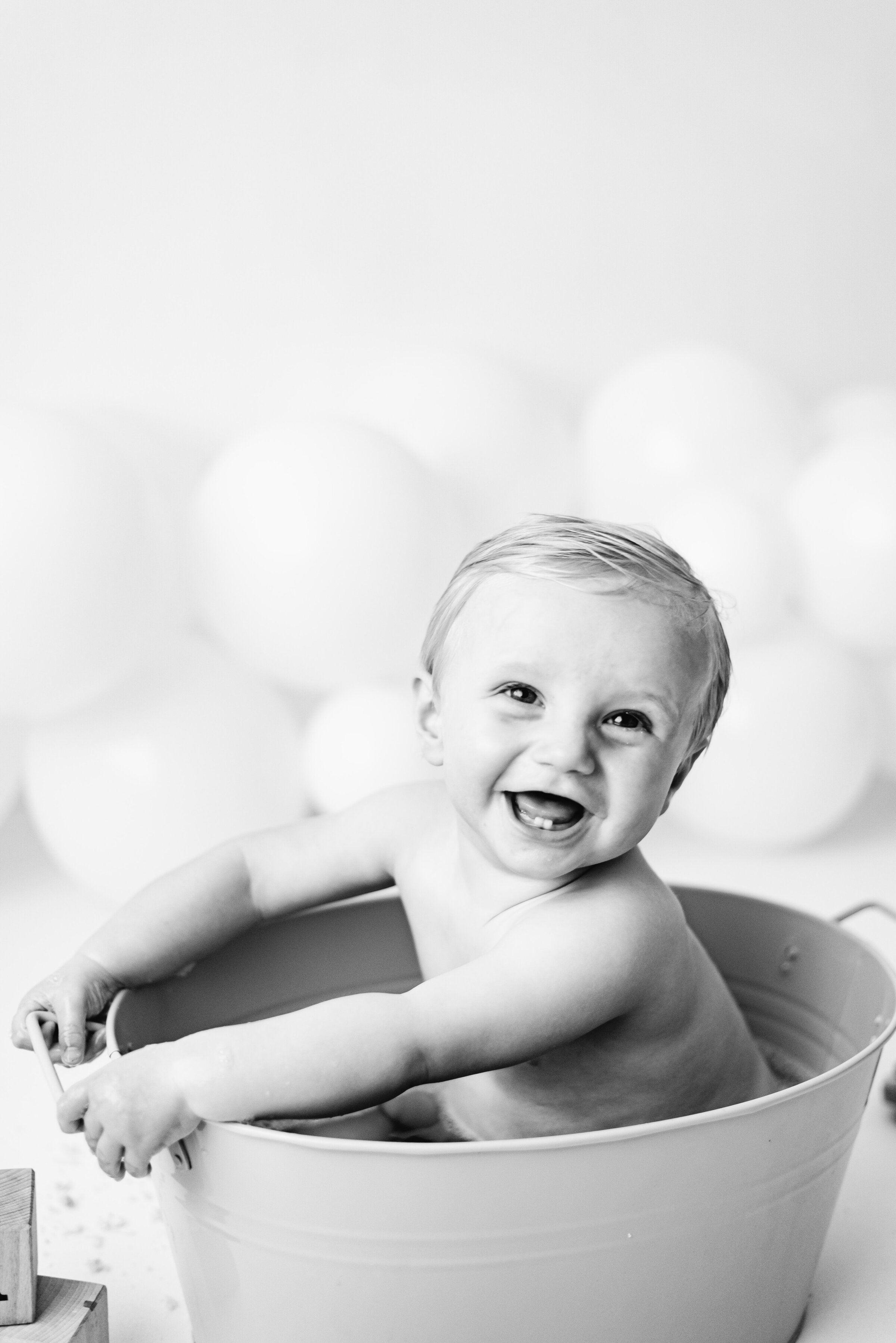 Baby boy sitting in a small bubble bath smiling at cake smash photoshoot in Billingshurst