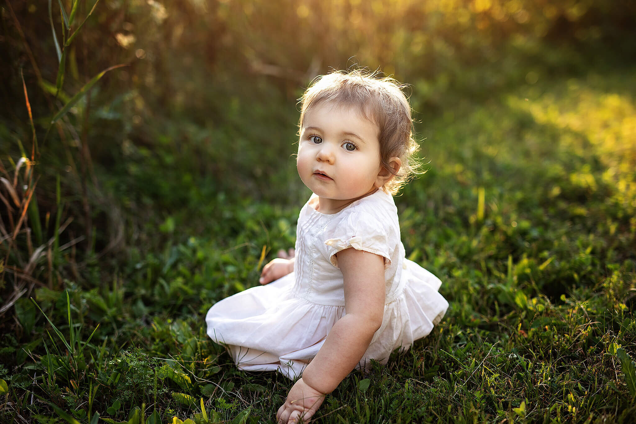 1 year old girl sitting in grass outside at lowe volk park