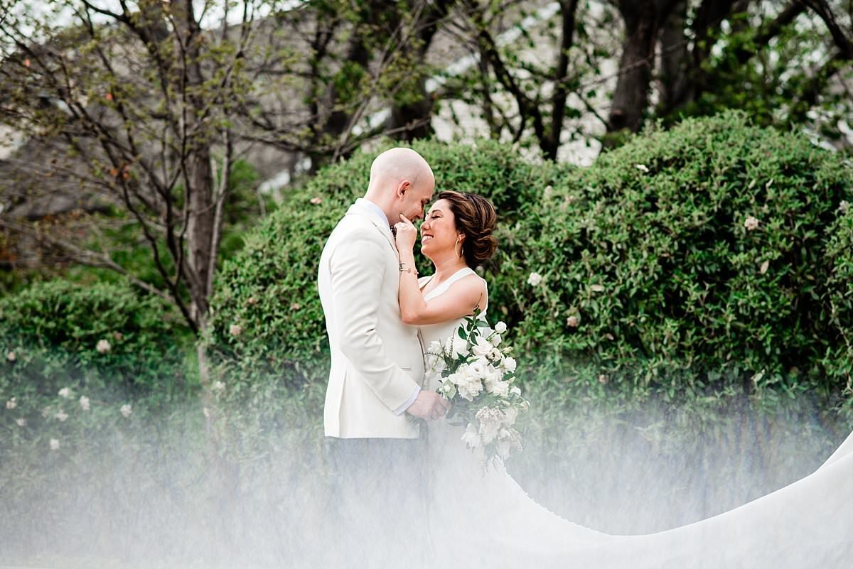 Portrait of bride and groom together near evergreen shrubs at Noah Liff Opera Center