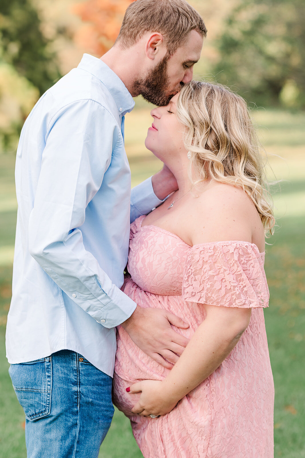 couple during maternity session in baltimore md park with dad kissing mom on the head and having a hand on her belly