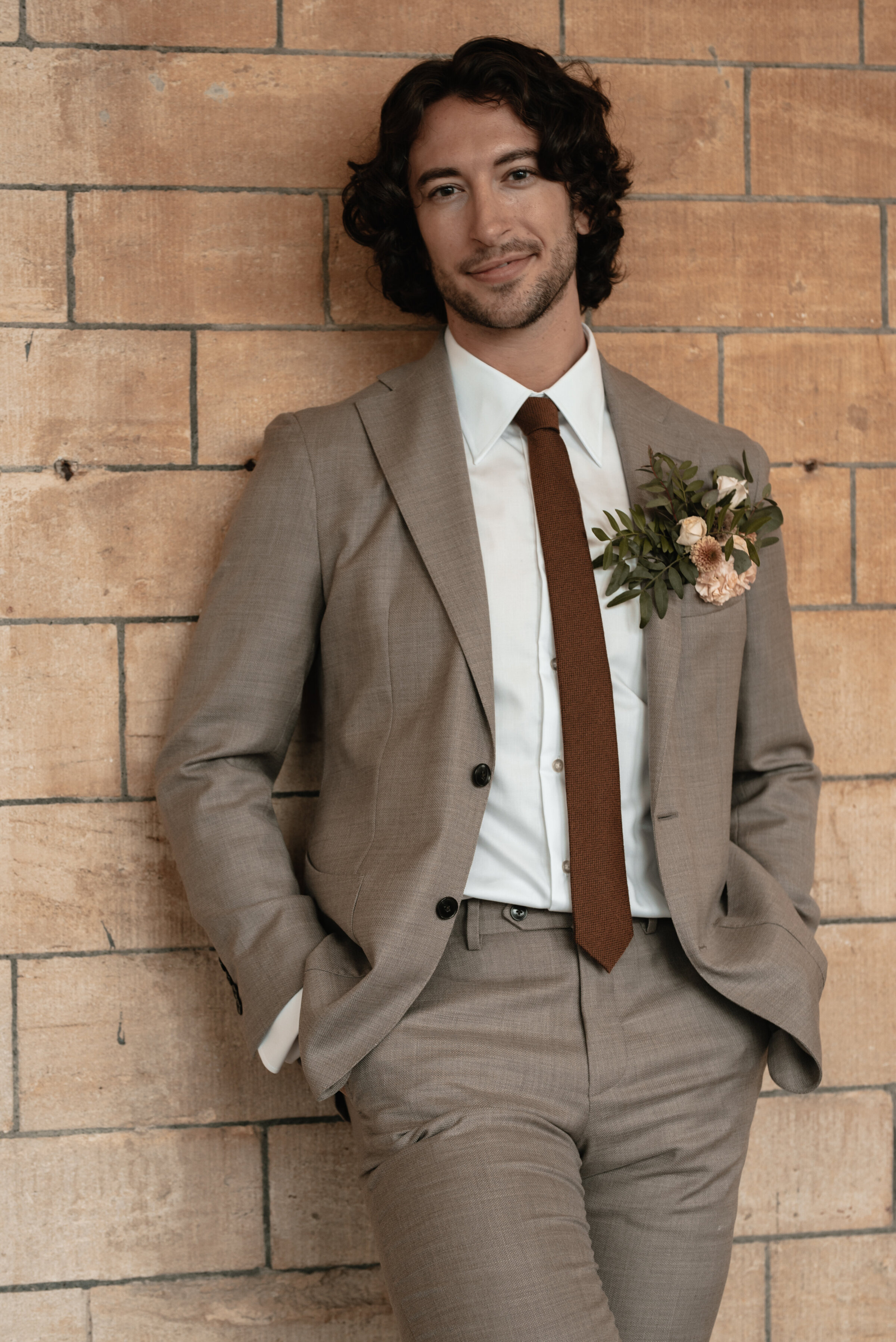 Groom in wedding suit standing with hands in pockets smiling directly at the camera