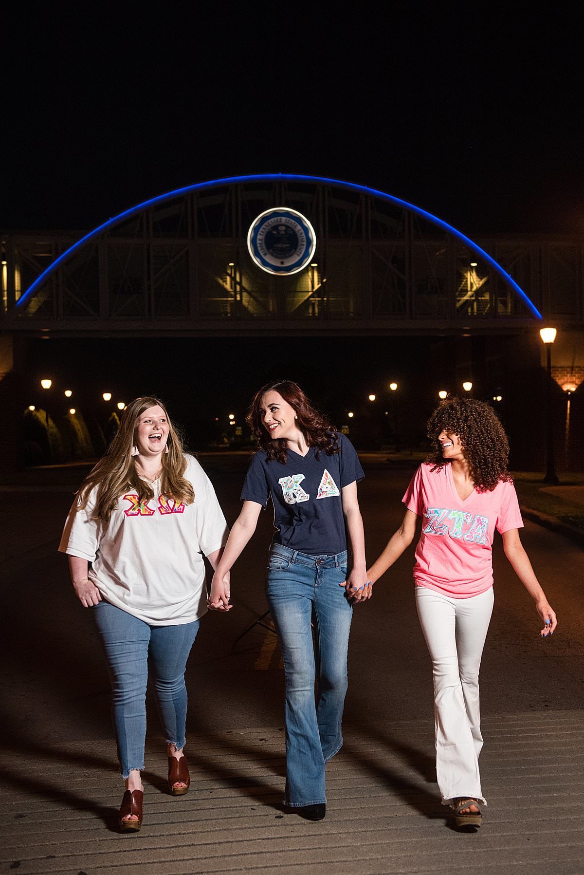 Chi Omega, Kappa Delta, and Zeta Tau Alpha  girls holding hands and walking at night near the bridge  on the Middle Tennessee State University campus