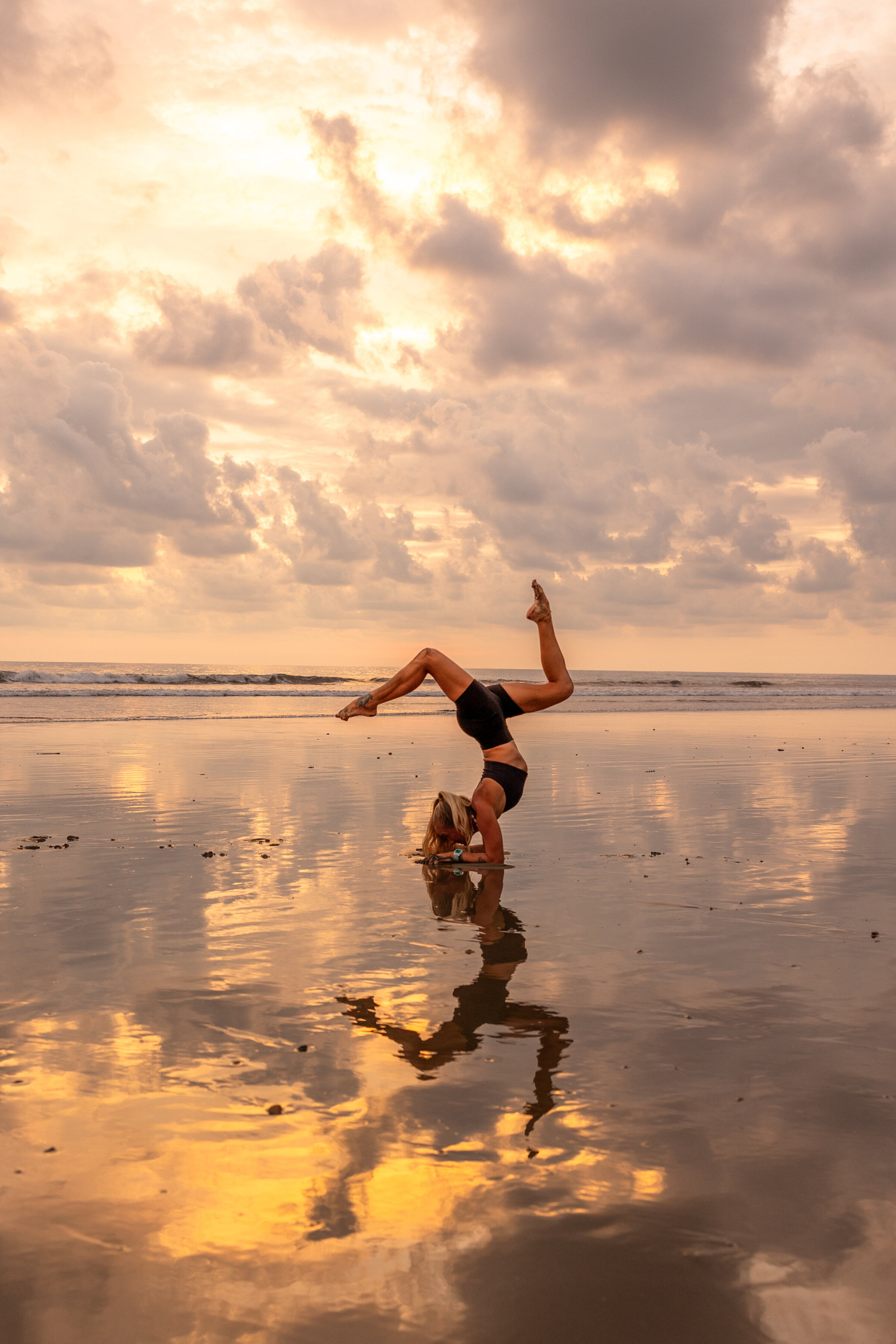 Woman doing handstand yoga pose on the beach shoreline at sunset