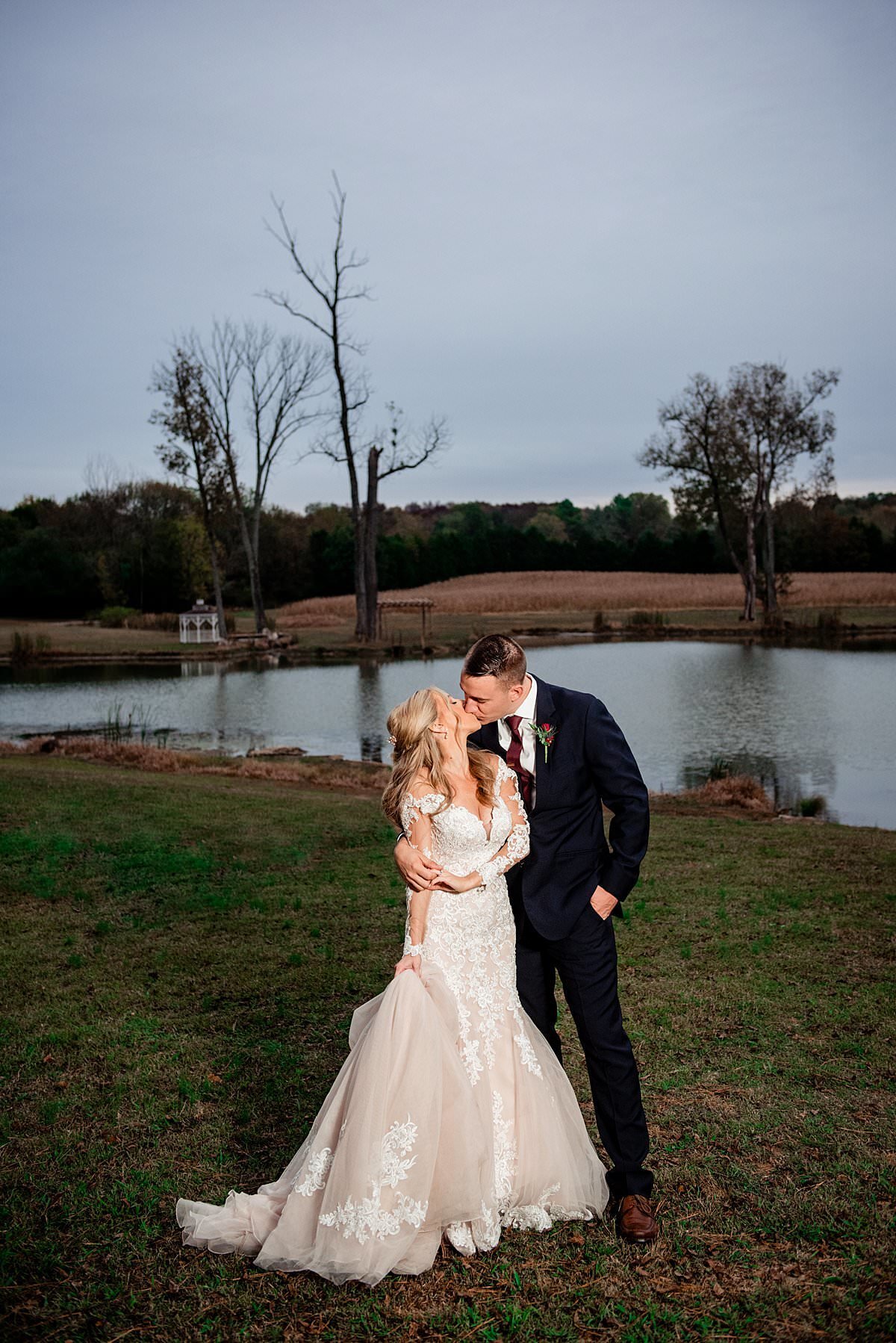 Romantic sunset wedding photo of bride and groom standing next to the pond at Rural Hill Farm