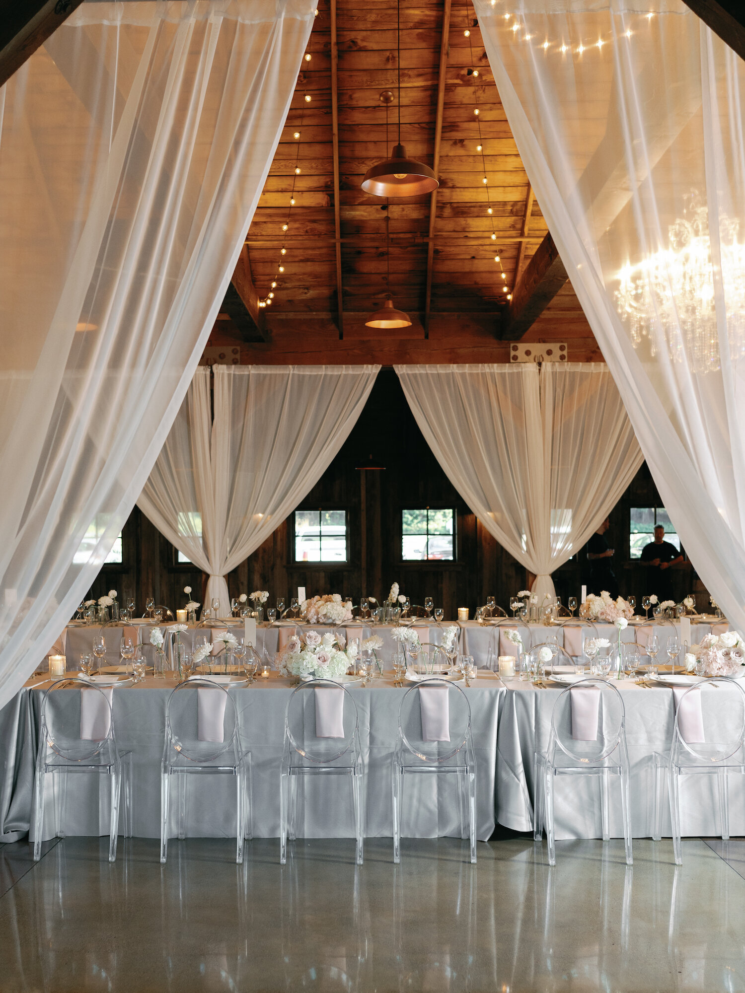 minimalist floral table-scape at wedding reception with ghost chairs in barn