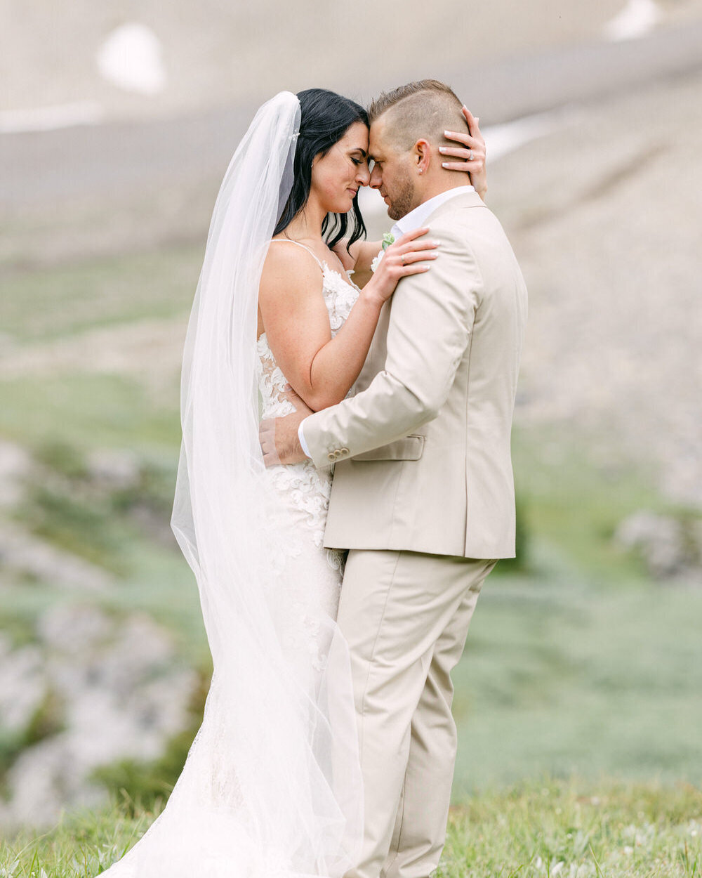 A breathtaking elopement photograph of the bride and groom embracing in the wild beauty of Mount Charles Stewart in Banff National Park. After arriving by private helicopter, they share a quiet, intimate moment, surrounded by the rugged peaks of the Canadian Rockies, making their adventure wedding truly unforgettable.
