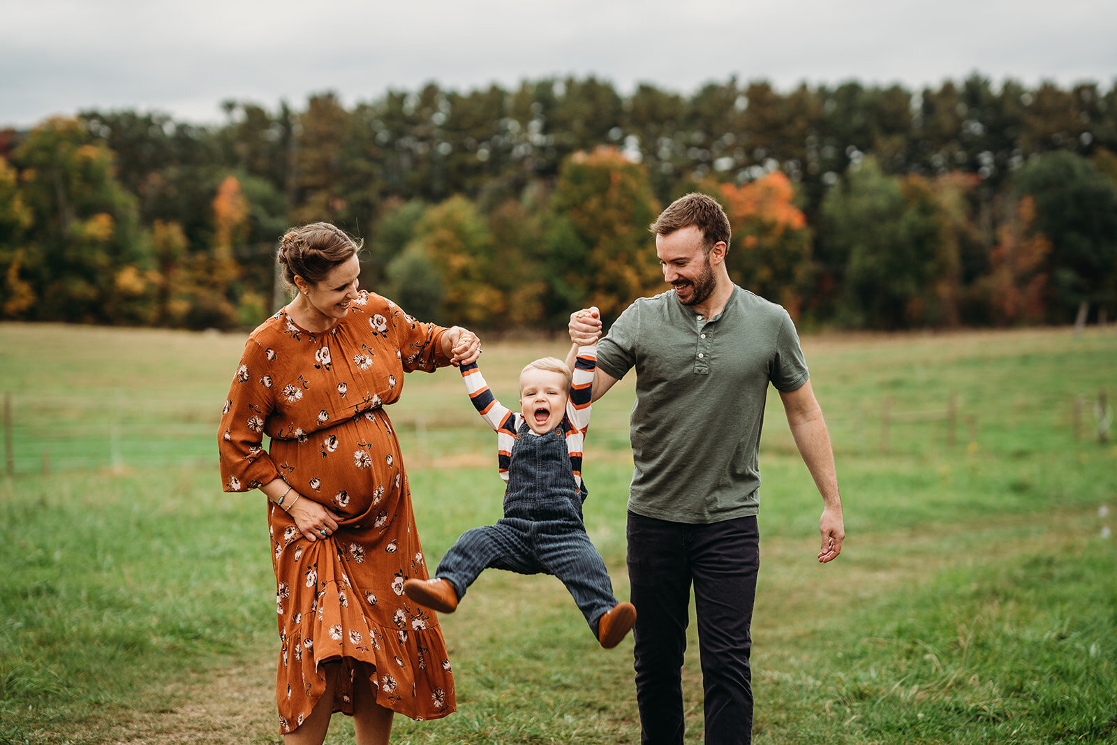 pregnant couple swings toddler boy in air during maternity pictures