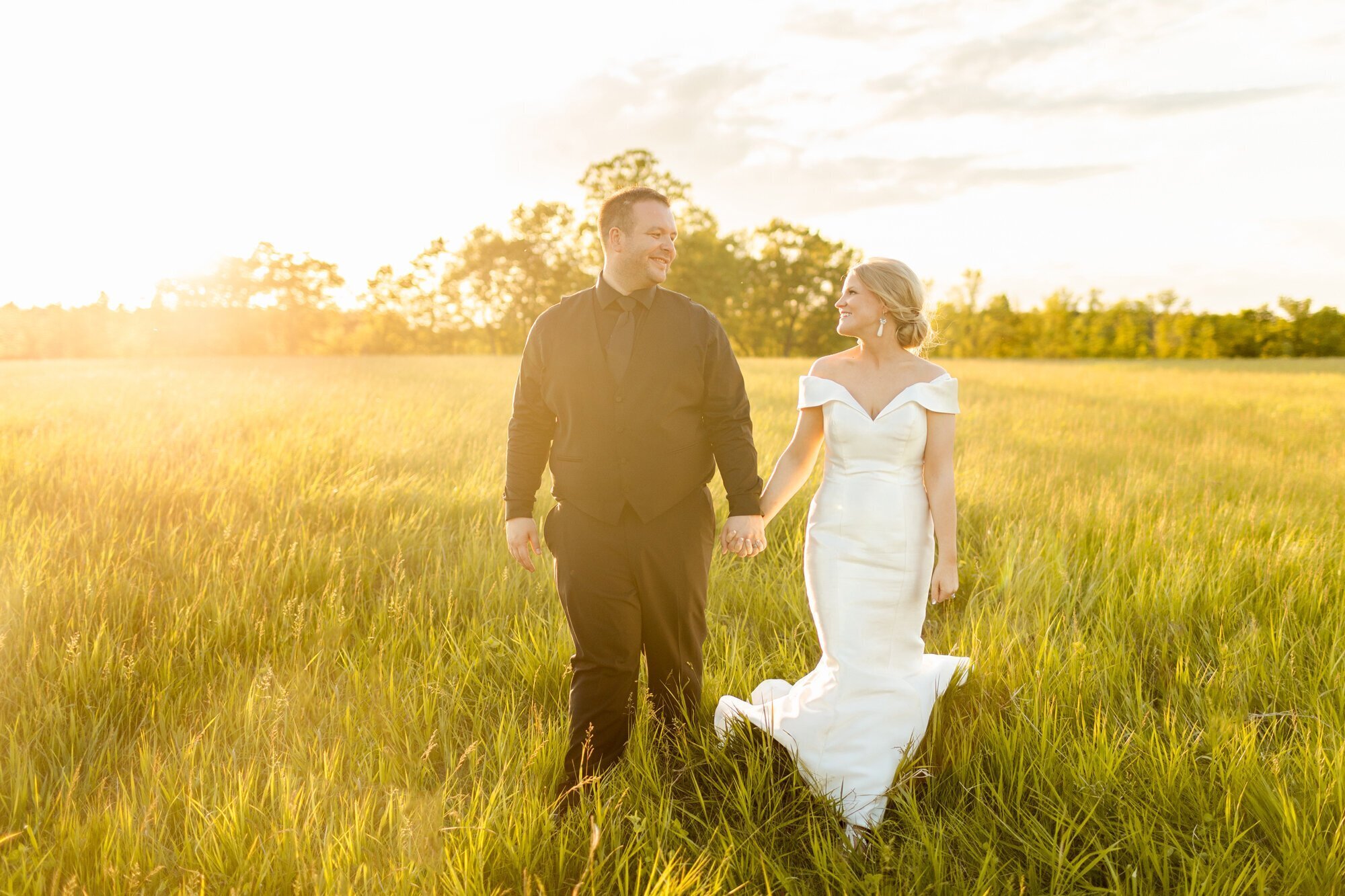 bride and groom holding hands and walking through field taken by wedding photographer minneapolis by Kacey Wyrick Photography