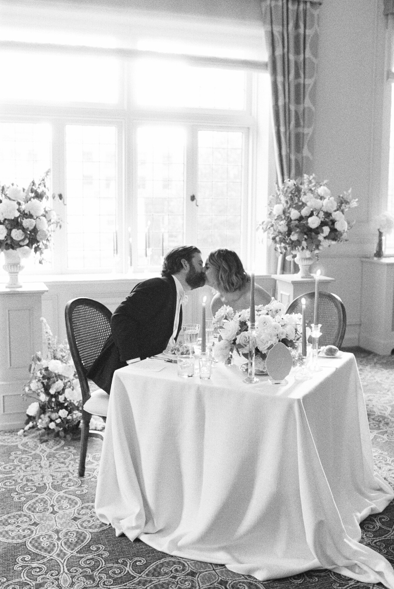 black and white 35mm film photo of bride and groom kissing at their wedding reception table