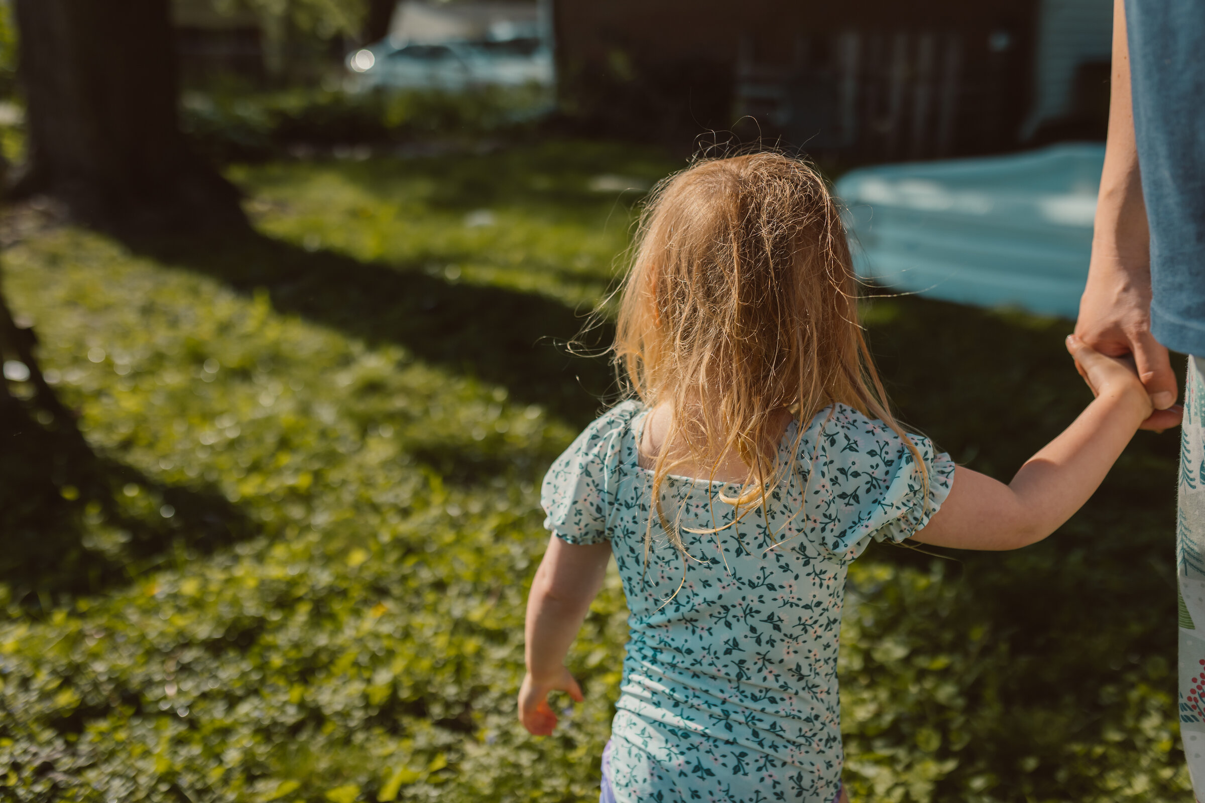 toddler girl faces away from the camera with wet messy hair wearing a swim suit holding her father's hand