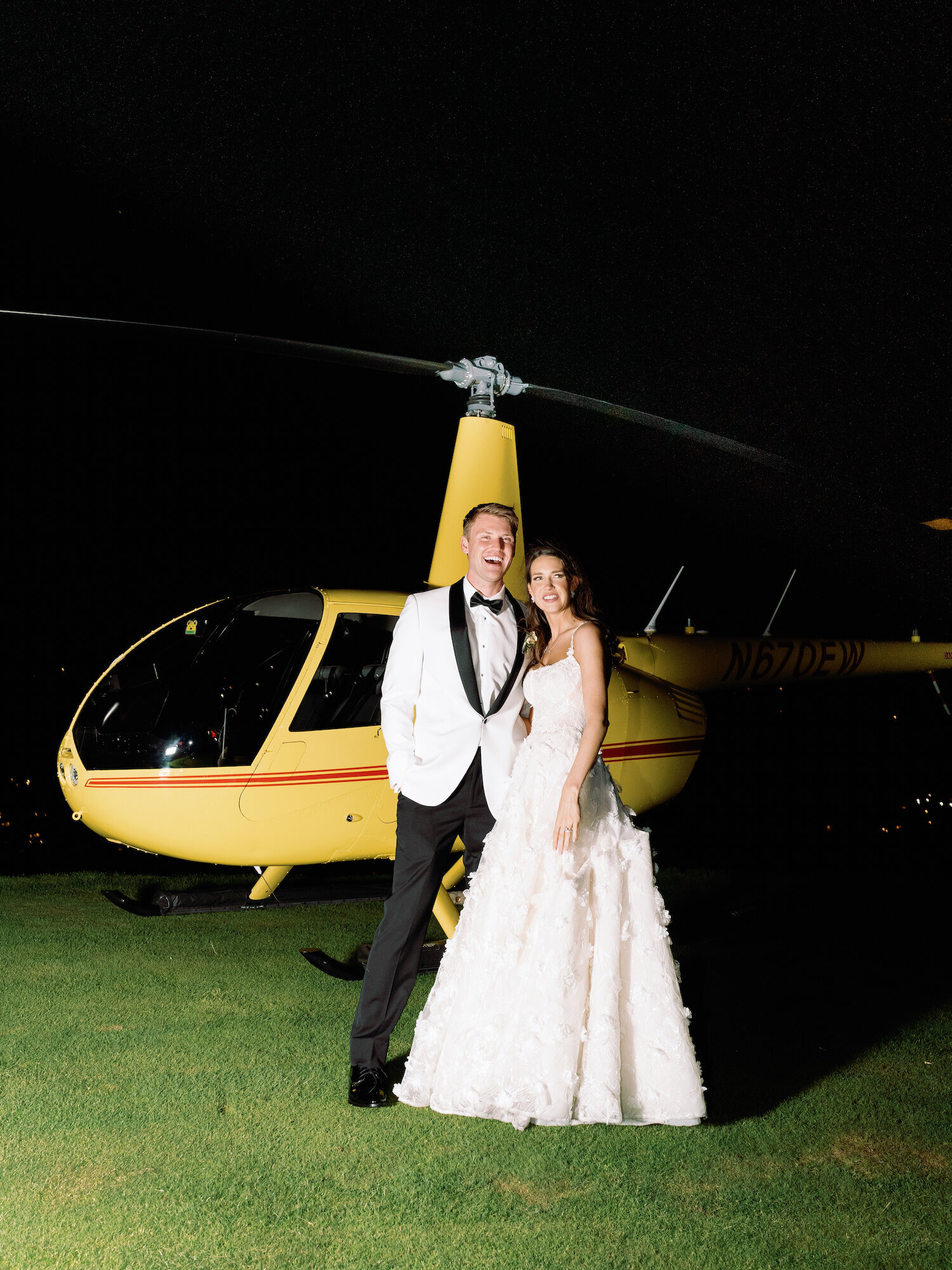 bride and groom smile in front of helicopter as they leave wedding