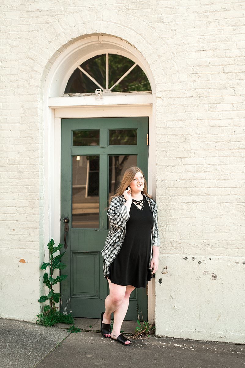 MTSU senior standing in green doorway wearing a black dress in downtown Murfreesboro