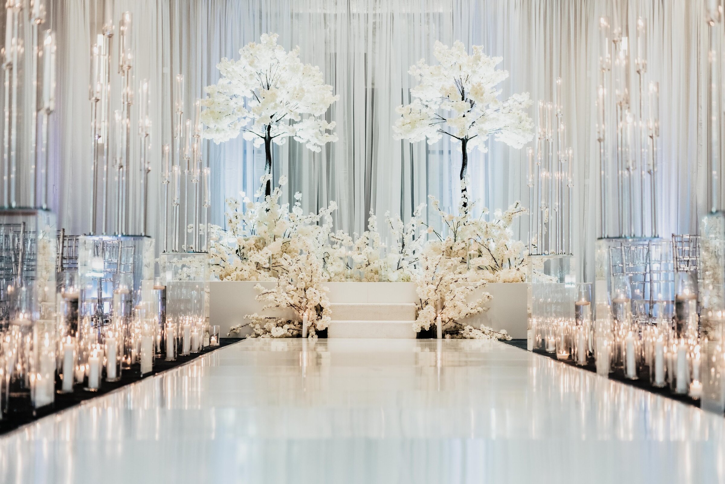 Luxurious white floral wedding ceremony at JW Marriott Nashville featuring cherry blossom trees, mirrored candle pillars, and elegant draping for a modern romantic look.