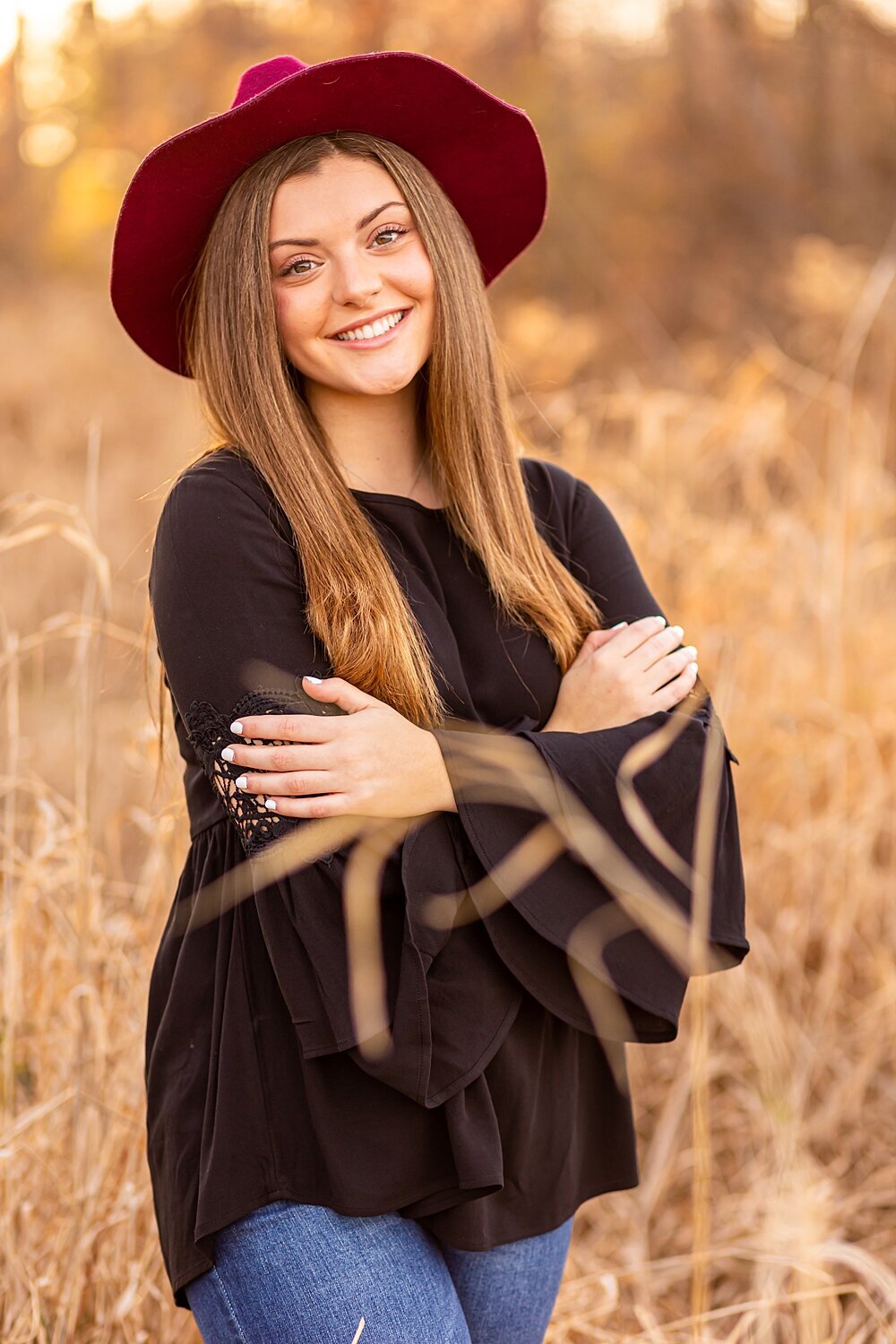 Fall senior girl folds arm and smiles in tall grass during fall senior session in Bedford, New Hampshire